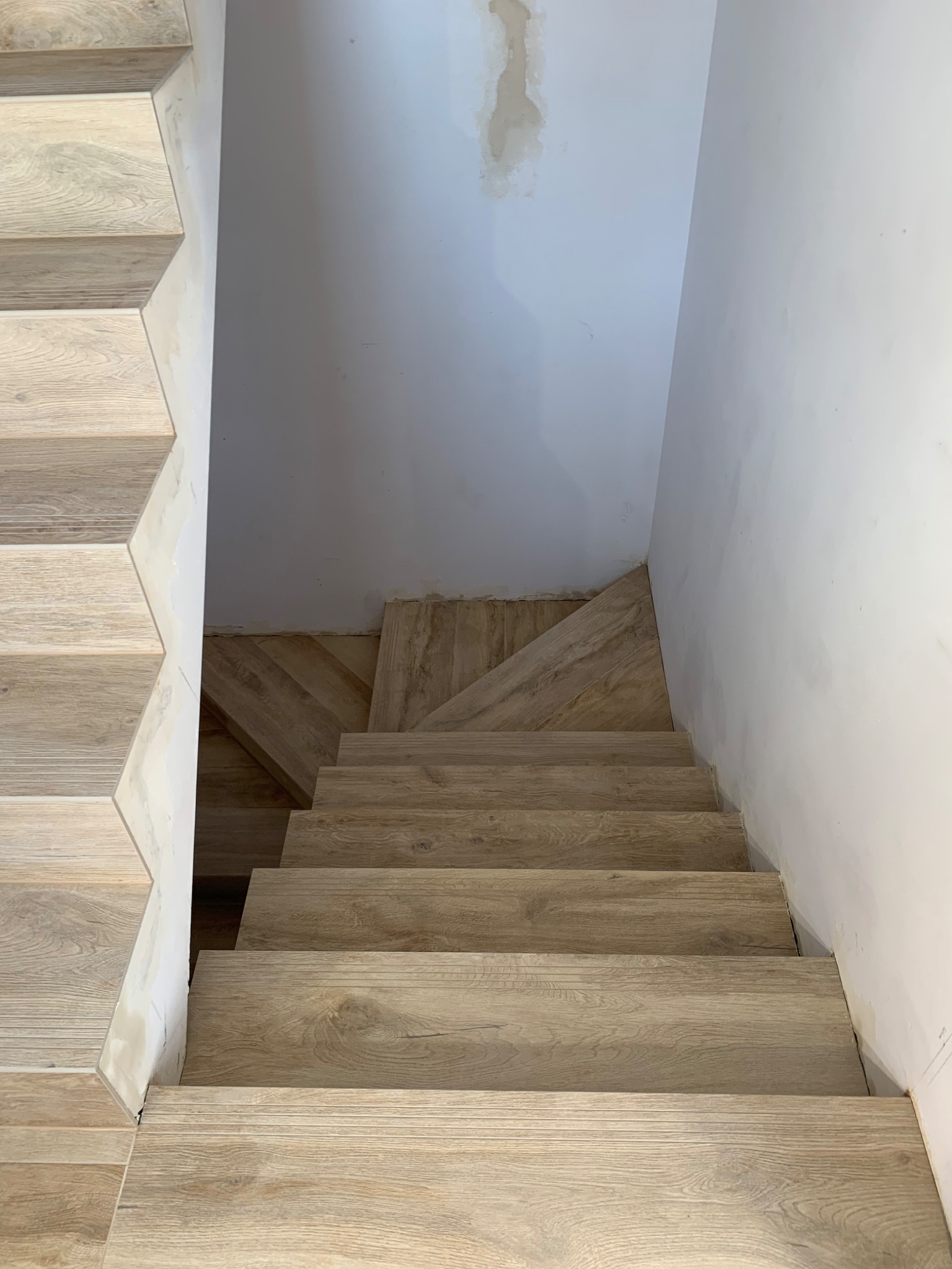 Schody wyłożone płytkami imitującymi drewno, widok z góry, ściany w trakcie wykończenia.