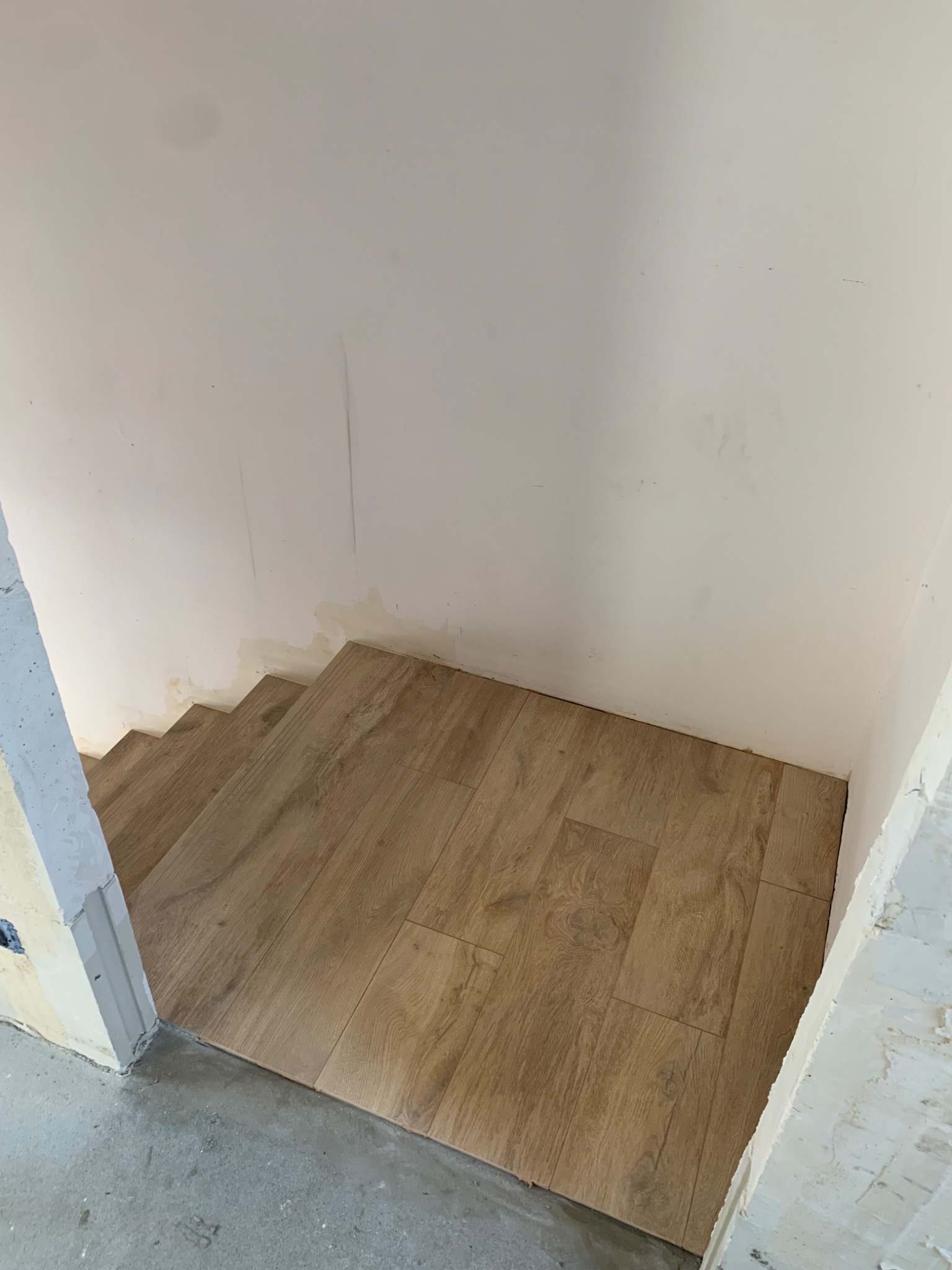 Układanie paneli imitujących drewno na schodach w trakcie remontu, widoczne niedoskonałości wykończenia ścian i surowy beton na podłodze.