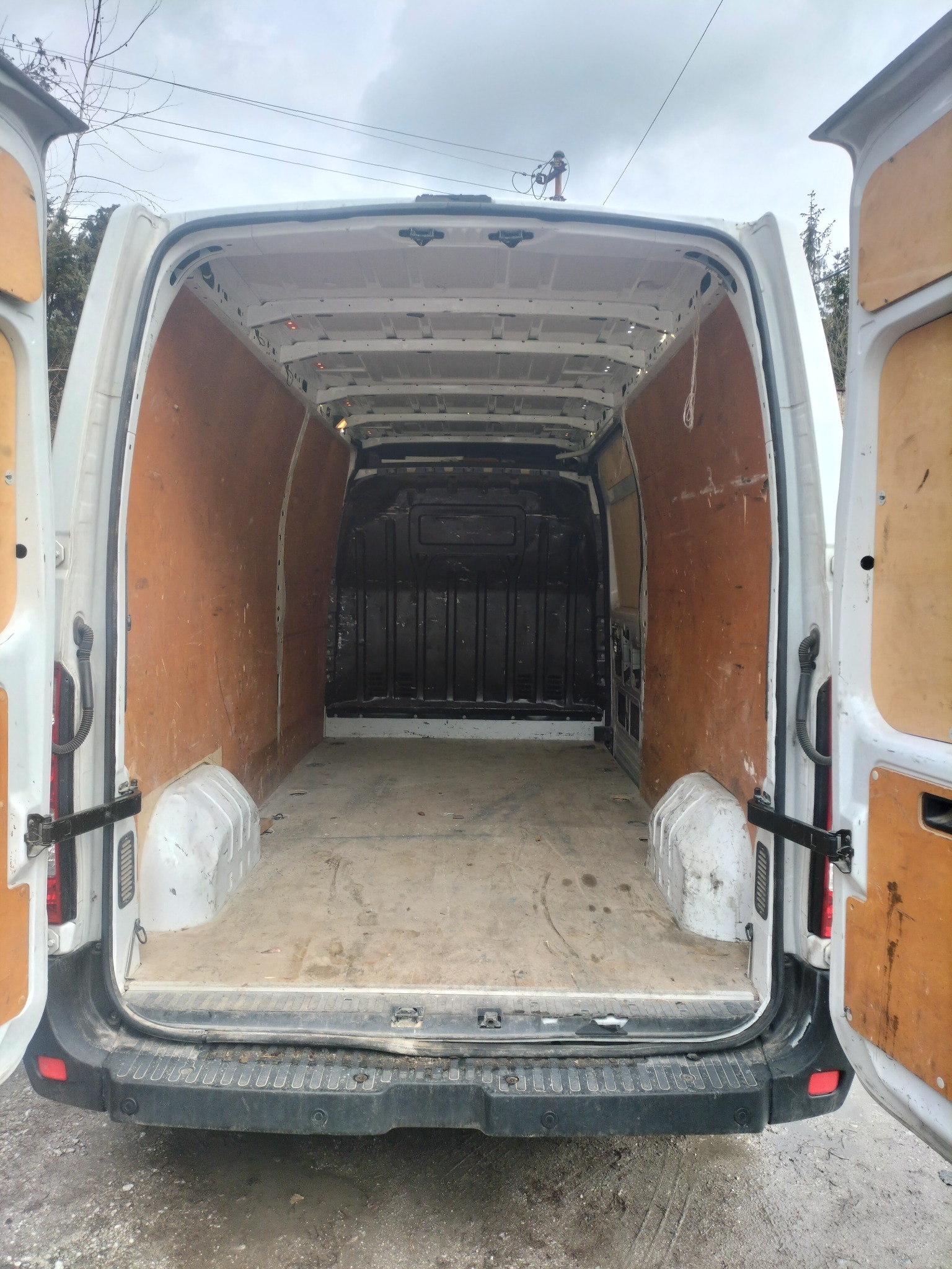 Wnętrze brudnego, pustego busa z otwartymi tylnymi drzwiami, widok od tyłu, ściany wyłożone płytami OSB, podłoga zakurzona.