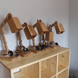 Woodluck - Cztery identyczne lampki biurkowe z jasnego drewna, z elementami sznurka i czarnymi kablami, stojące na drewnianej szafce z otwartymi półkami.