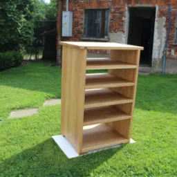 Drewniana szafka z półkami ustawiona na trawie przed ceglanym budynkiem z oknami.