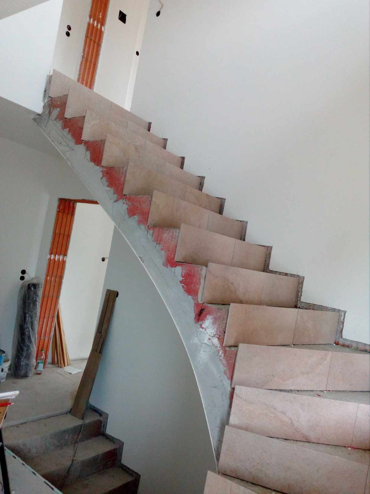 Schody w trakcie wykańczania, z widocznymi płytkami w odcieniach beżu i czerwonymi śladami zaprawy, z niezabezpieczonymi przewodami elektrycznymi w tle.