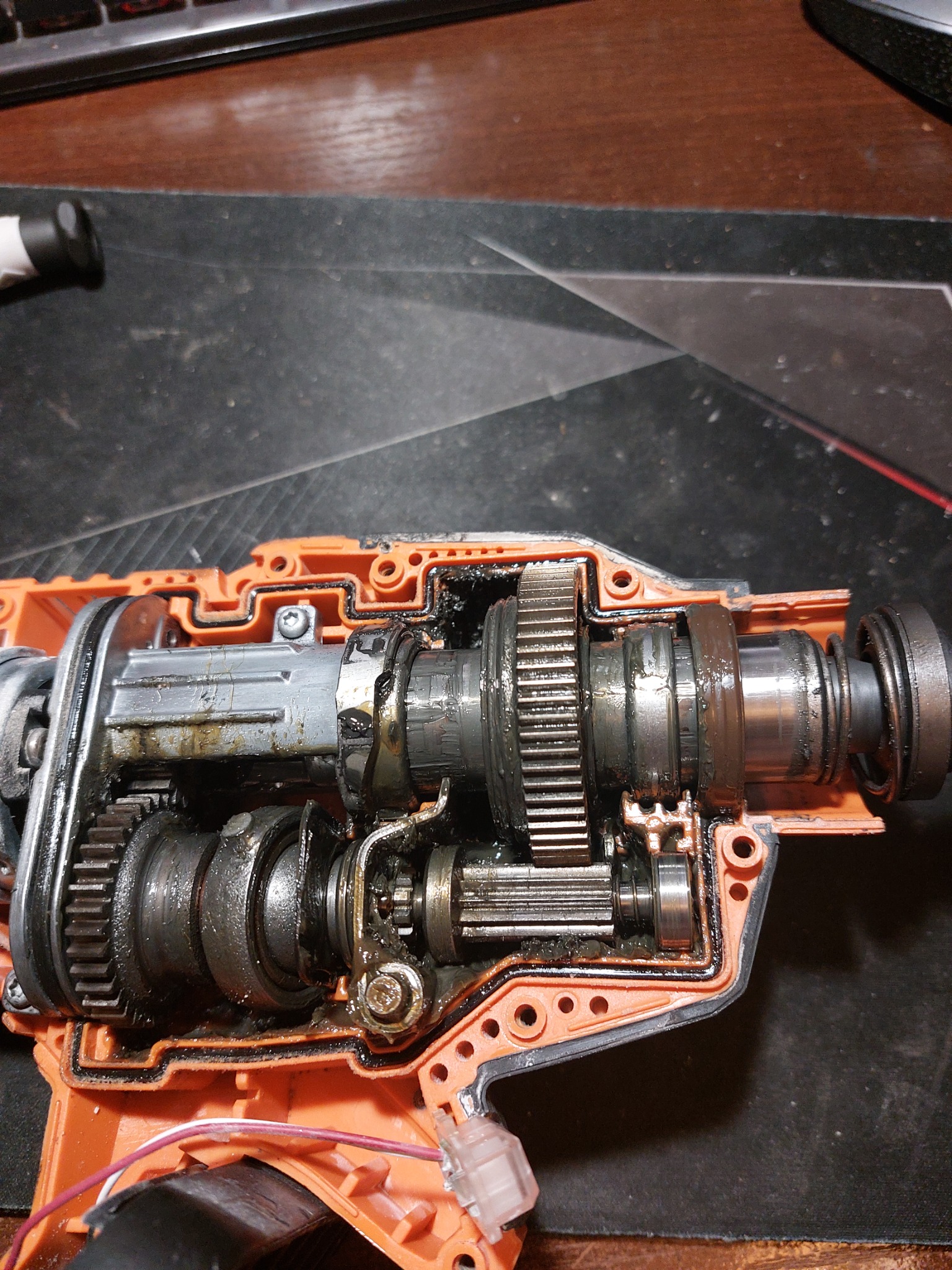 Wnętrze przekładni pomarańczowej obudowy urządzenia budowlanego, widoczne metalowe zębatki i elementy mechaniczne pokryte smarem.