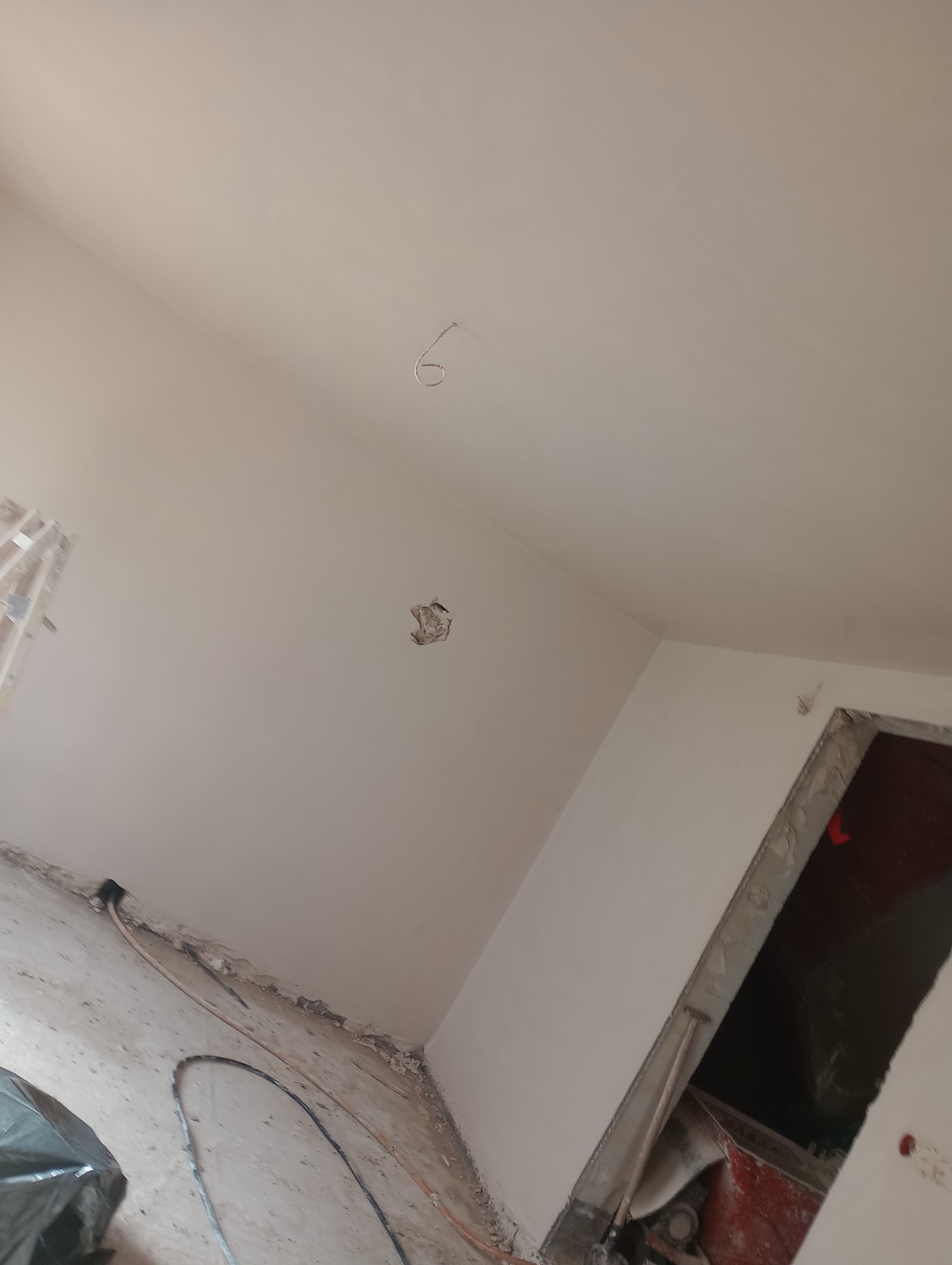 Wnętrze w trakcie remontu; ściany i sufit po nałożeniu gładzi, widoczne niedoskonałości i otwór w ścianie, kabel wystający z sufitu, podłoga z resztkami gruzu i kablami.