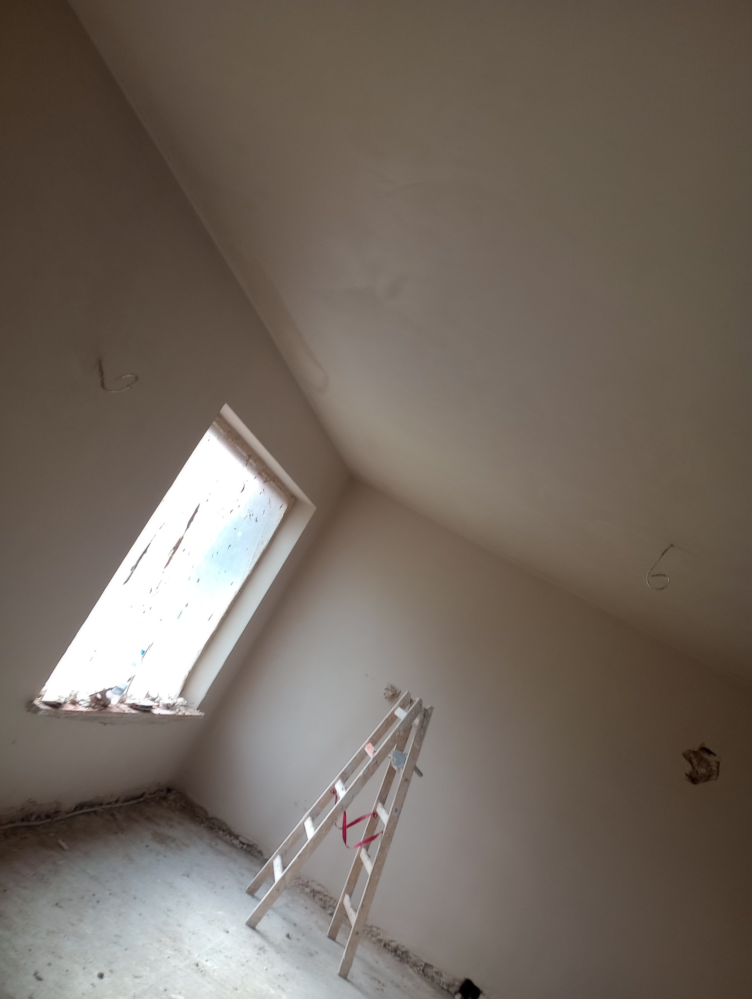 Poddasze w trakcie remontu: ściany i skośny sufit po nałożeniu gładzi, drewniana drabina oparta o ścianę, widoczne niedokończone obramowanie okna dachowego.