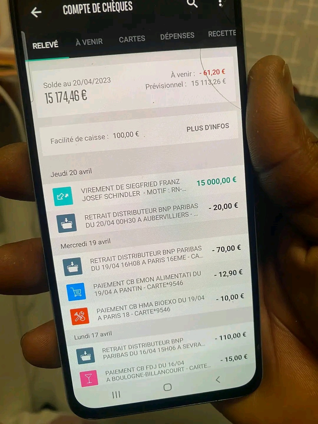 Ekran smartfona z otwartą aplikacją bankową prezentującą historię transakcji i saldo konta w euro, widoczny pęknięty ekran w górnej części.