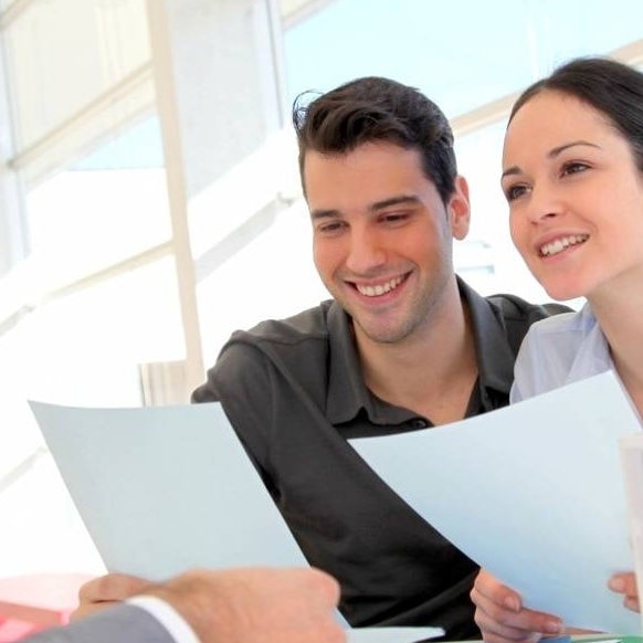 Uśmiechnięta para analizuje dokumenty kredytowe z doradcą, widoczne jasne, nowoczesne biuro w tle.