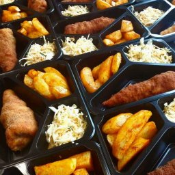 Pogotowie Gastronomiczne - Zestaw dań w czarnych, trójdzielnych pojemnikach: kotlet schabowy, ziemniaki pieczone z przyprawami i surówka z kapusty, ułożone w rzędach, gotowe do transportu.