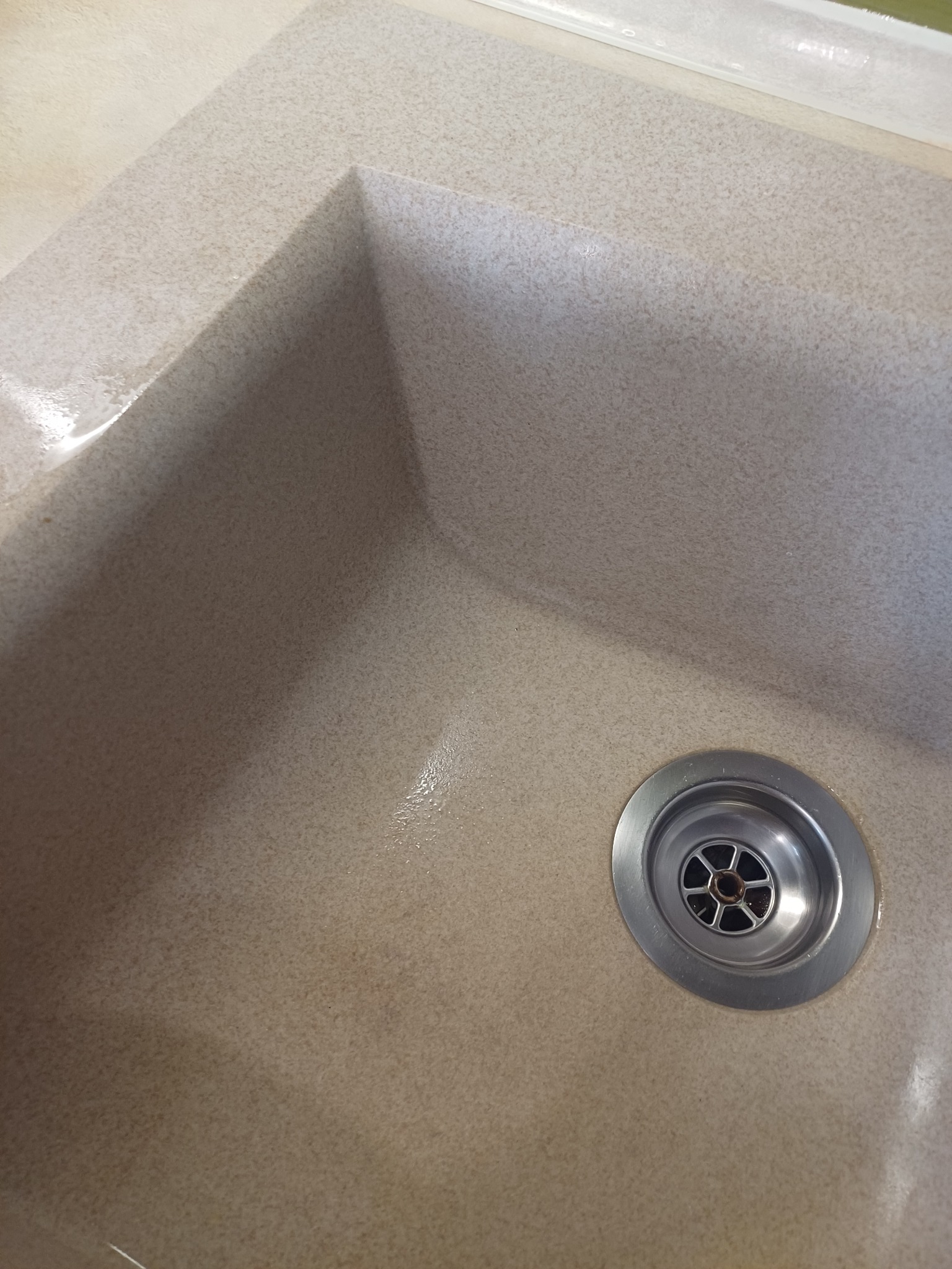 Beżowy, kwadratowy zlew z odpływem ze stali nierdzewnej, widoczne ślady wilgoci po czyszczeniu.