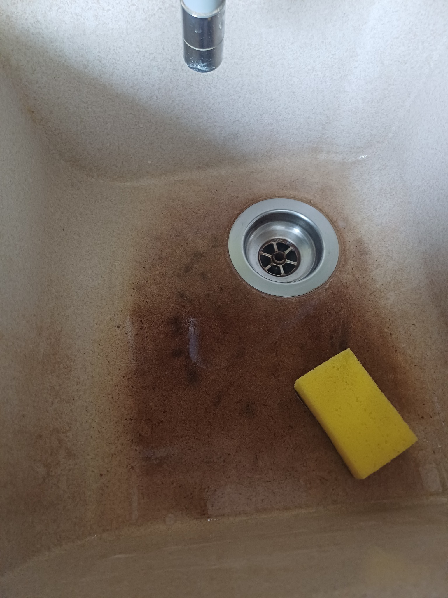 Zabrudzony zlew z żółtą gąbką, widoczne ślady po zaciekach i osadzie, kran w górnej części kadru.