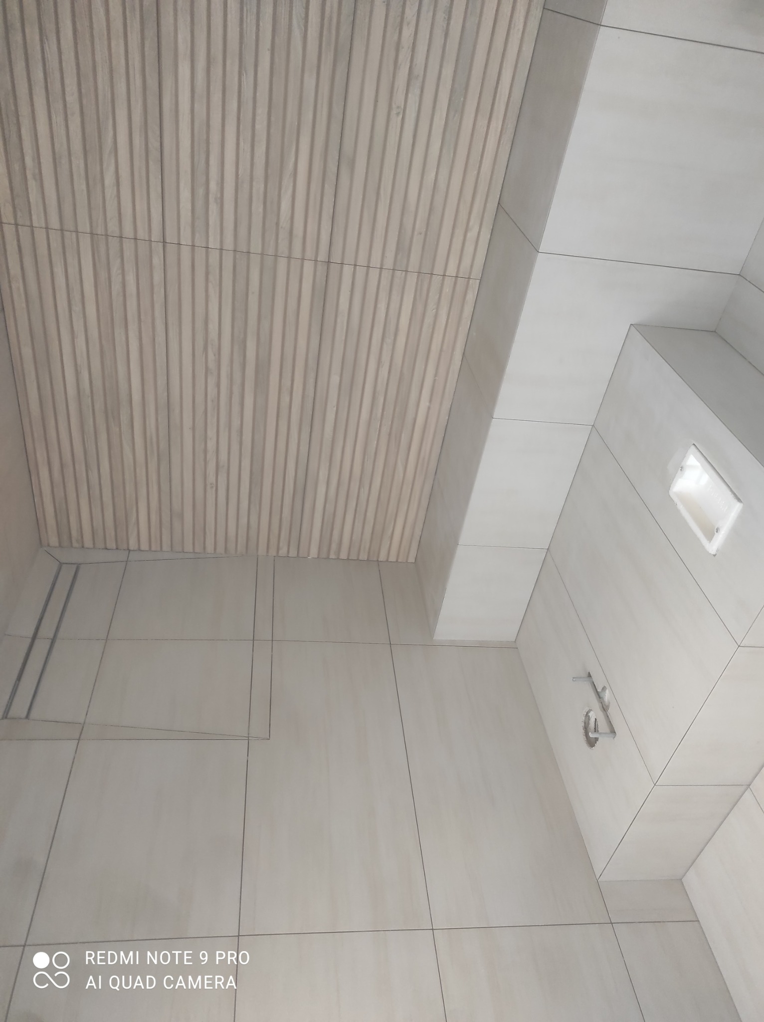 Nowoczesna łazienka z drewnopodobnym panelem na suficie, jasne płytki na ścianach i podłodze, minimalistyczna armatura.