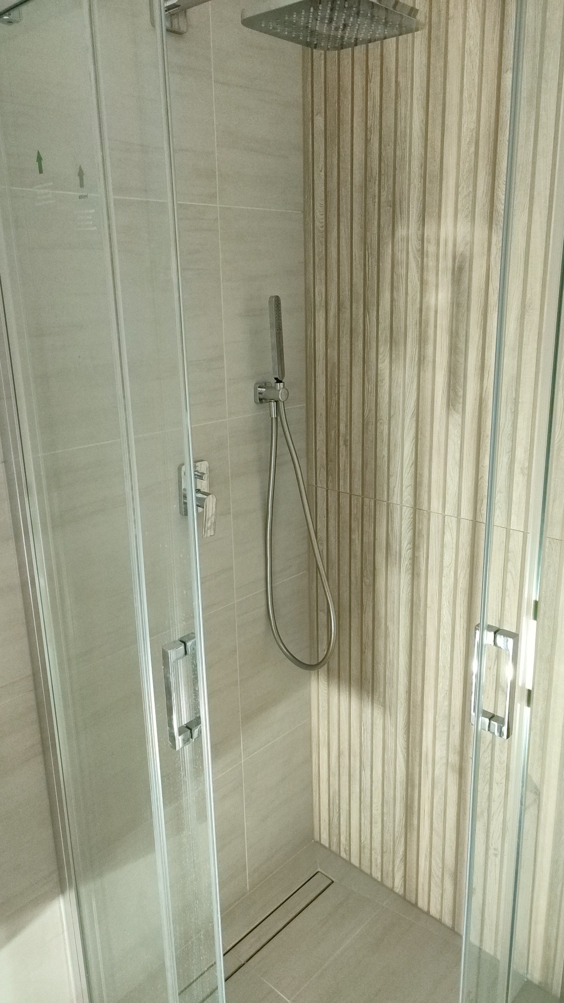 Nowoczesna kabina prysznicowa z deszczownicą i panelami ściennymi imitującymi drewno, widoczny odpływ liniowy w podłodze.