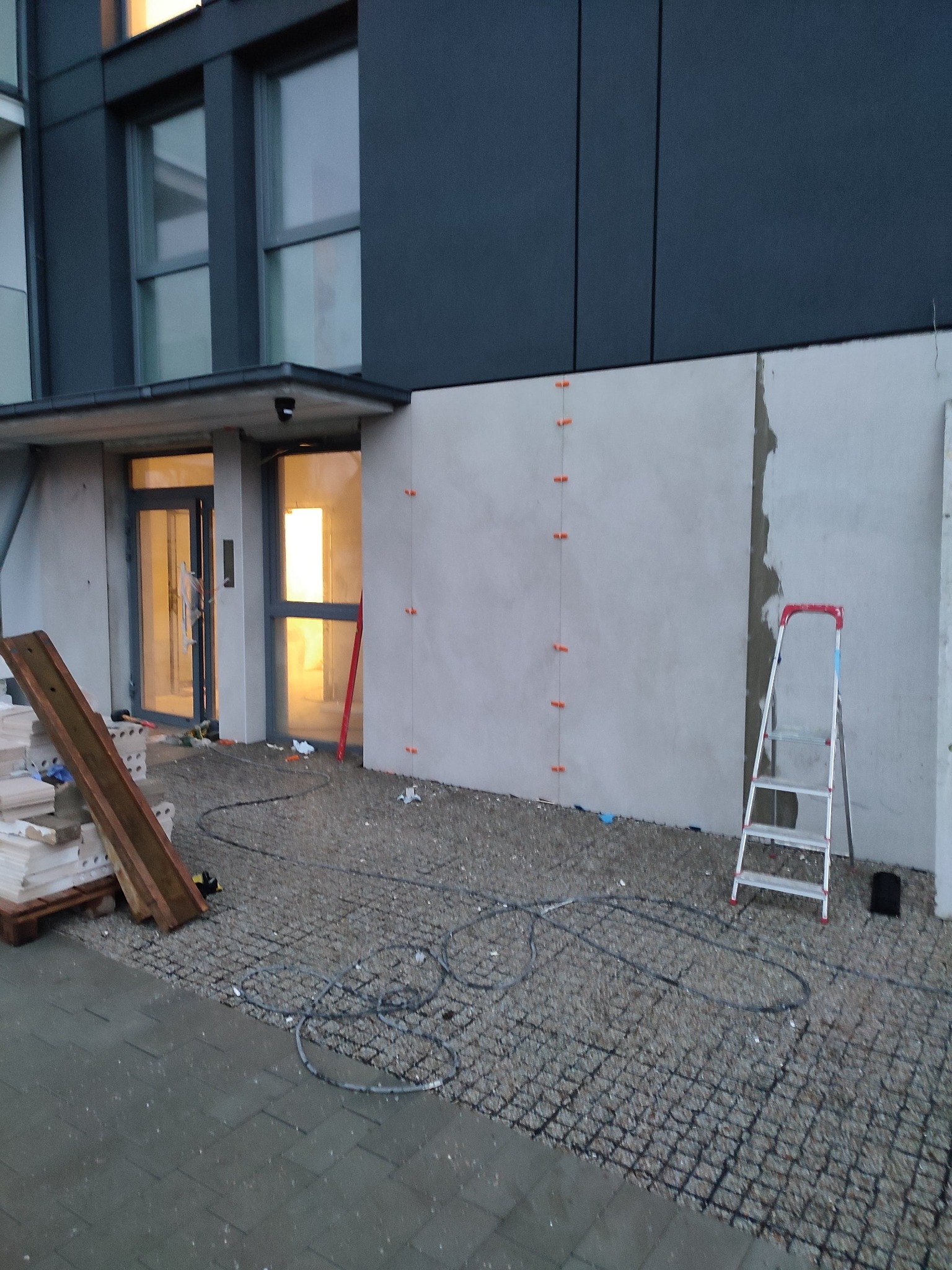 Elewacja budynku w trakcie wygładzania, widoczne listwy prowadzące, drabina aluminiowa i materiały budowlane.