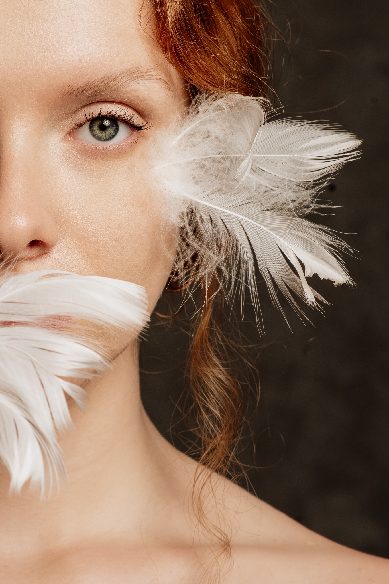 Portret kobiety z rudymi włosami, z piórami zakrywającymi część twarzy, skupiający się na zielonym oku i delikatnej skórze.