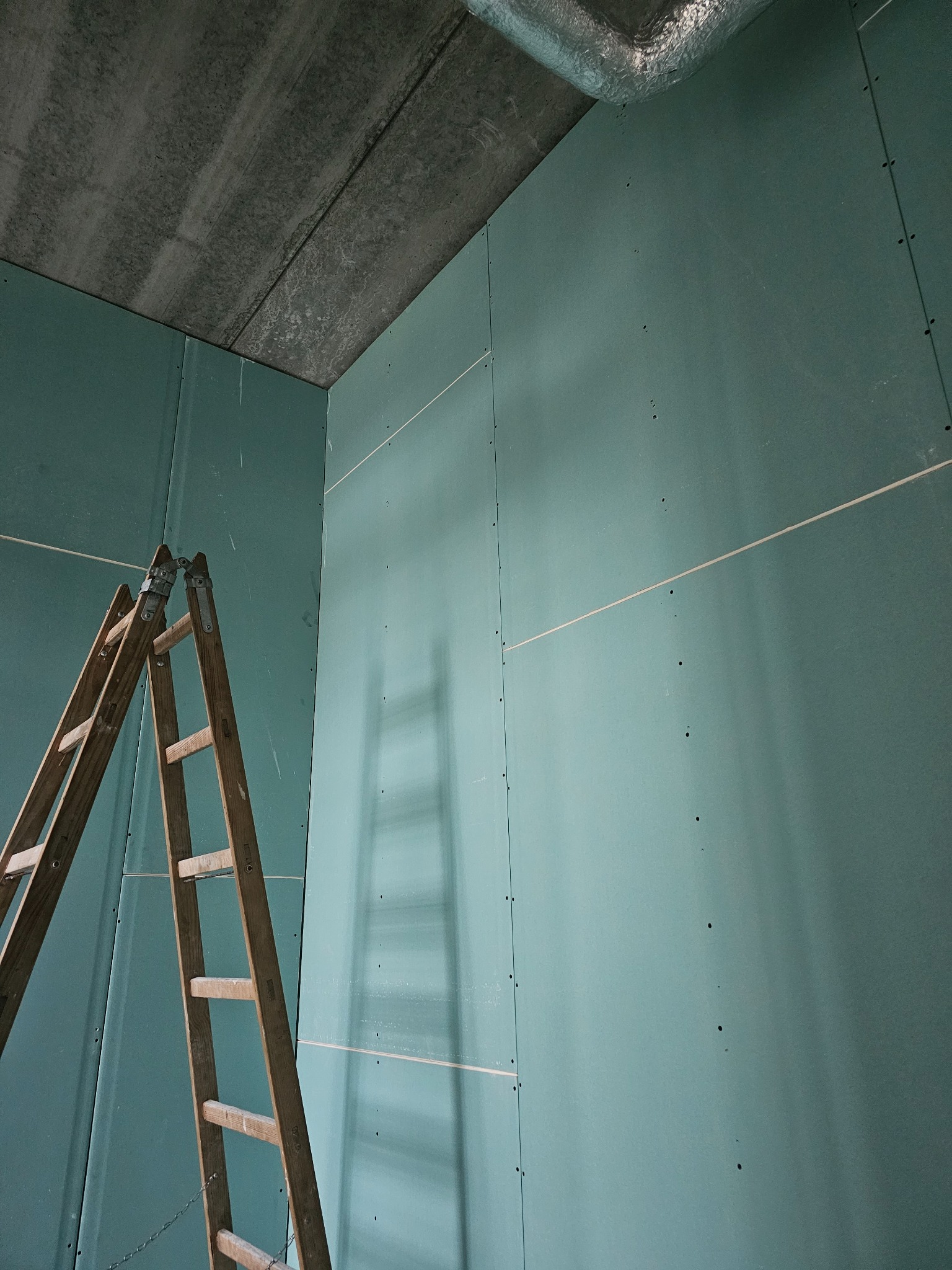 Ściana z zielonej płyty karton-gips, zamocowana na stelażu, widoczna drabina drewniana w trakcie prac wykończeniowych w Warszawie.