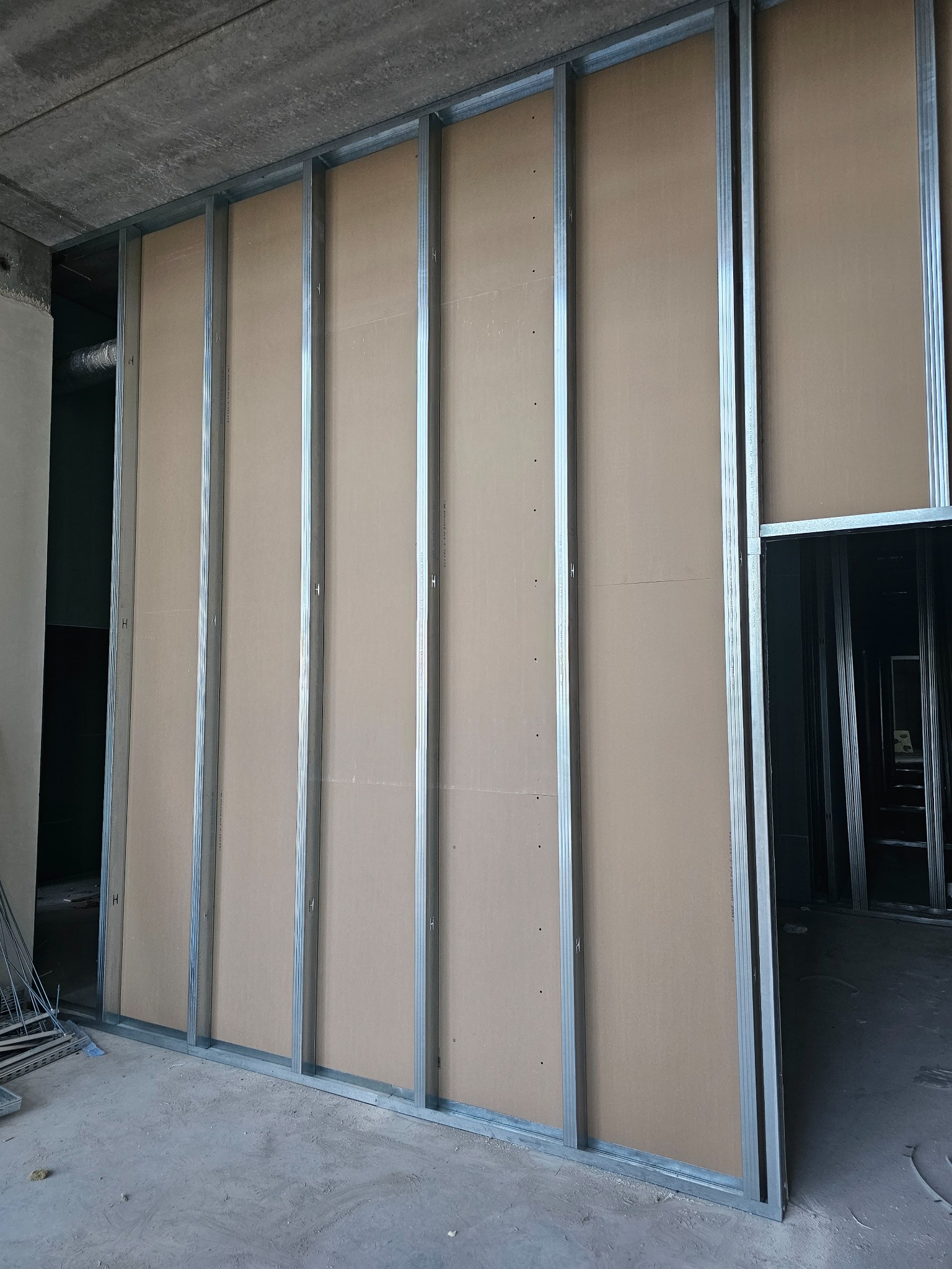 Konstrukcja ścian działowych z płyty karton-gips na metalowym stelażu, widoczny etap montażu, surowy betonowy strop w tle.