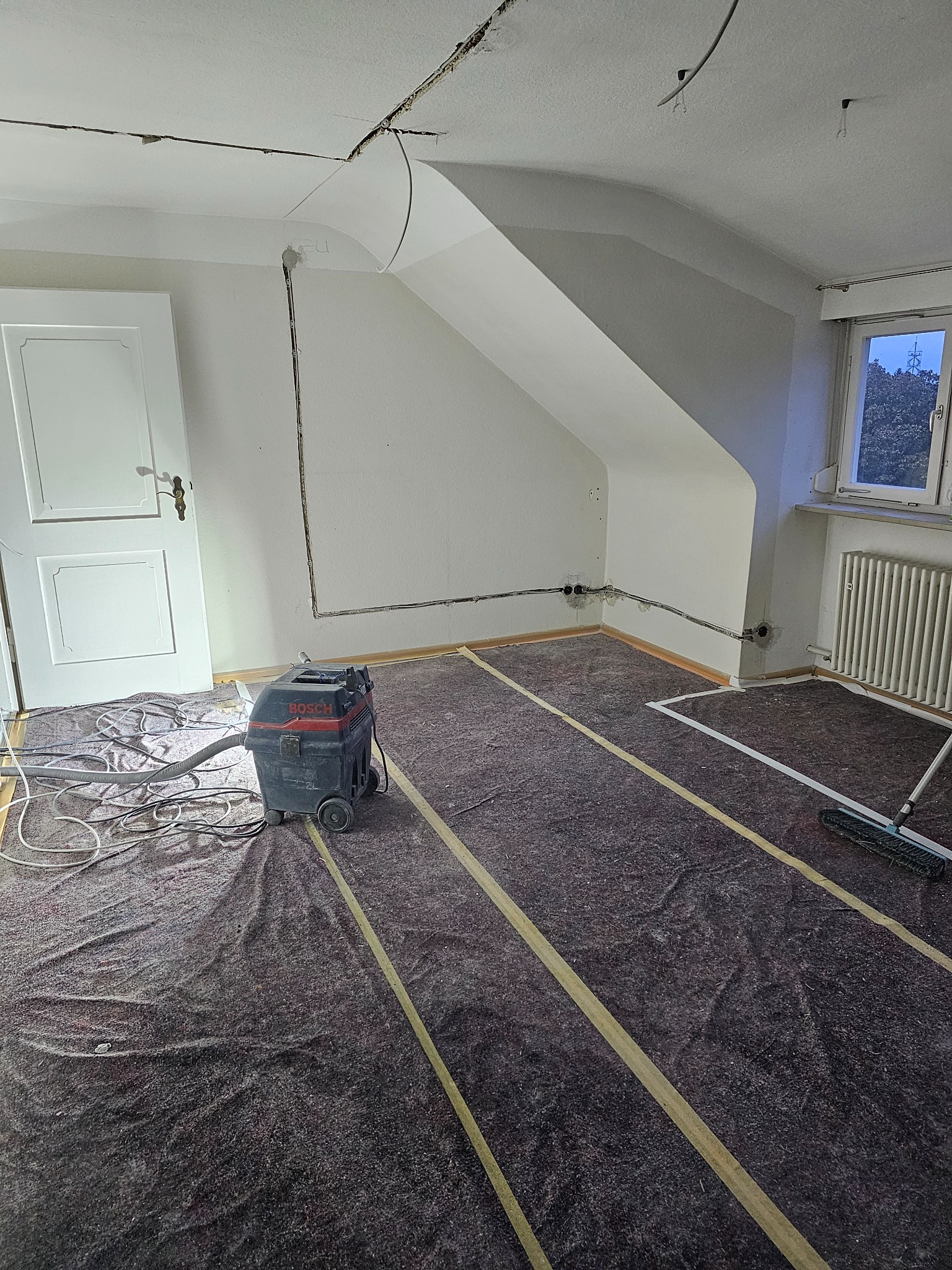 Pokój w trakcie prac przygotowawczych do remontu: zabezpieczona podłoga, poprowadzone kable w ścianach, widoczny odkurzacz przemysłowy Bosch i szczotka.