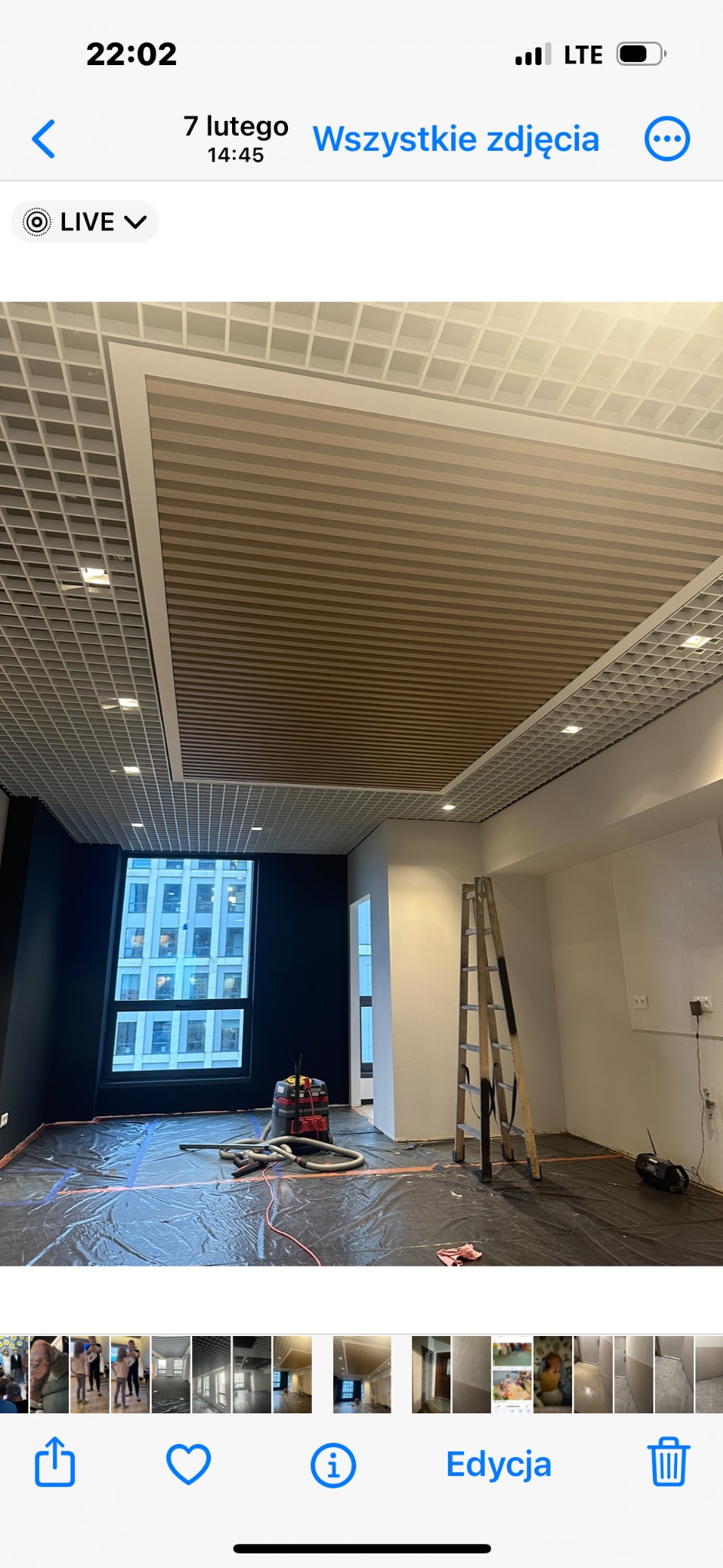 Biuro w trakcie remontu z zabezpieczoną folią podłogą, widocznym odkurzaczem przemysłowym, drabiną i nowym kasetonowym sufitem z elementami drewnianymi.