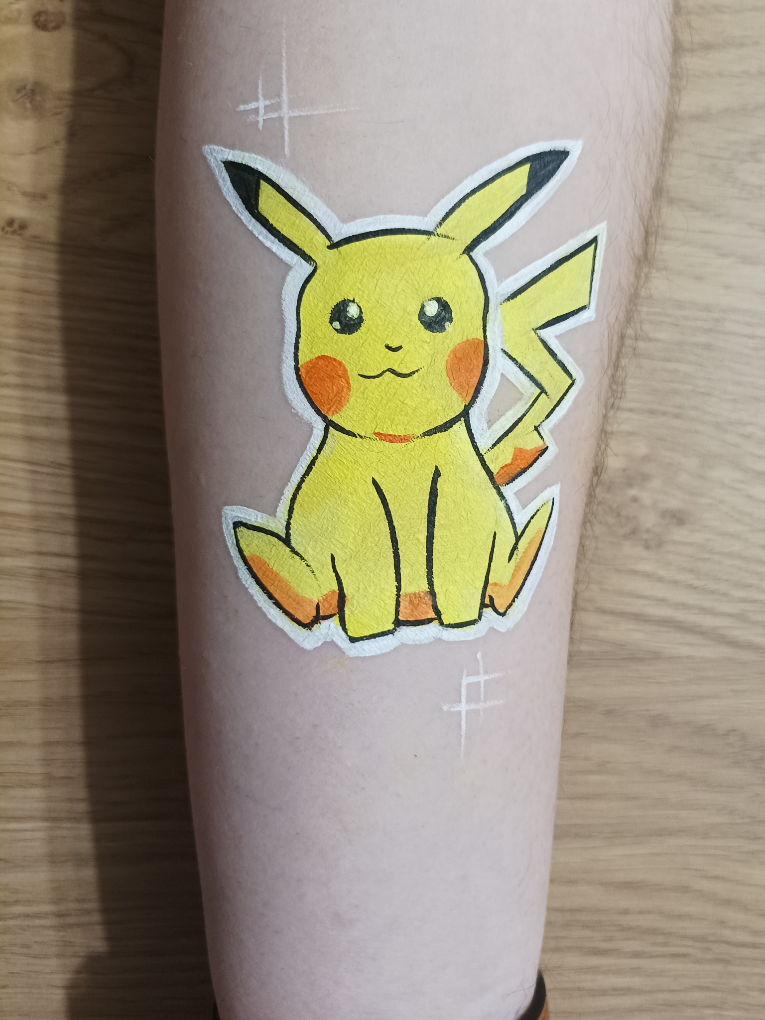 Malunek na nodze przedstawiający postać Pikachu z Pokemonów, wykonany farbami do ciała z białym obrysem i dodatkowymi białymi znakami.
