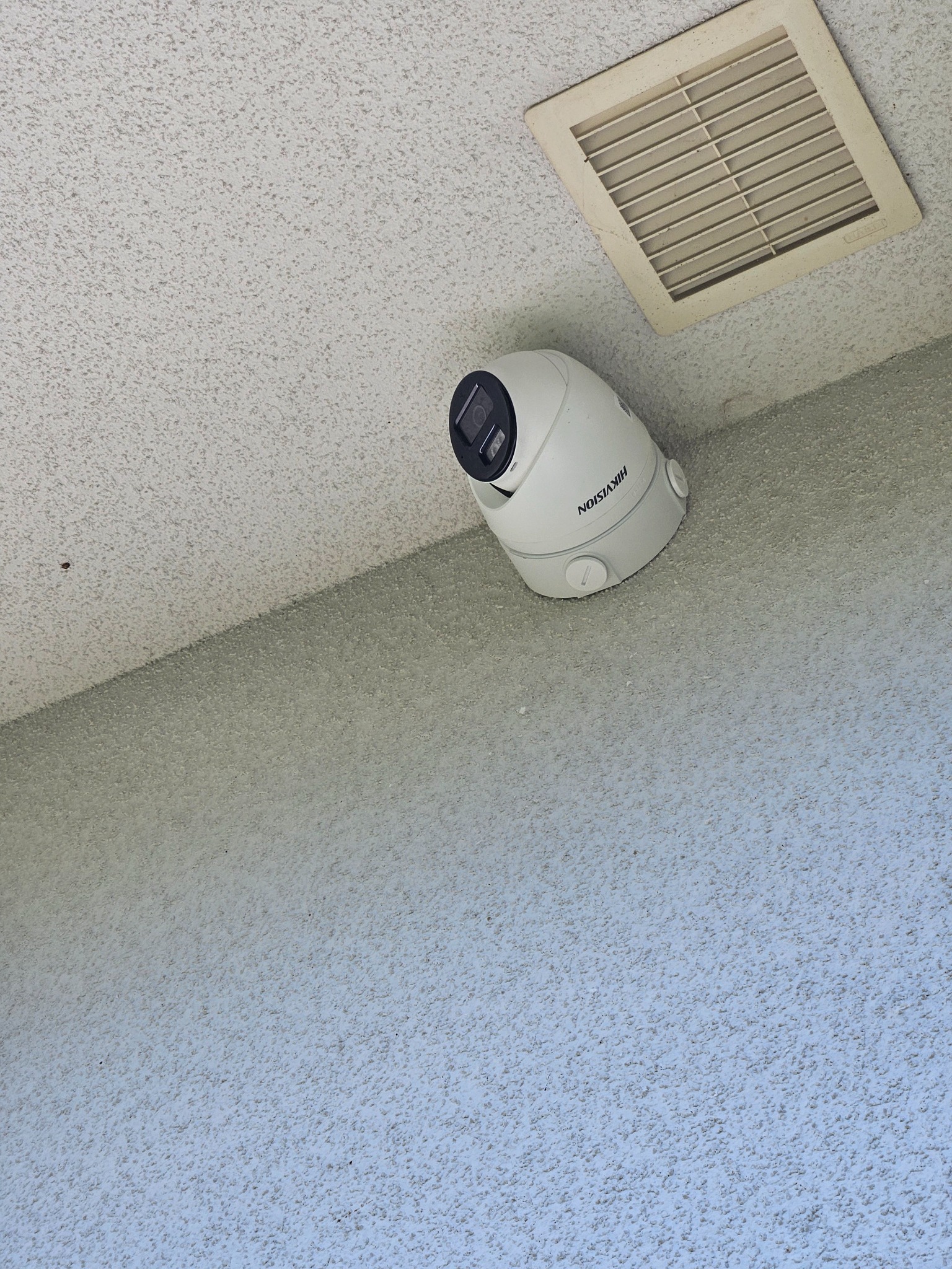 Kamera obrotowa Hikvision zamontowana na suficie z fakturą baranka, obok kratka wentylacyjna.