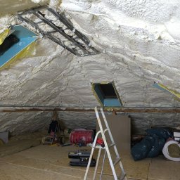 Hubert Gurzyński PUR-DOM - Poddasze po natrysku izolacji piankowej, widoczne okna dachowe i elementy konstrukcyjne. Izolacja pokrywa całą powierzchnię, tworząc jednolitą warstwę.