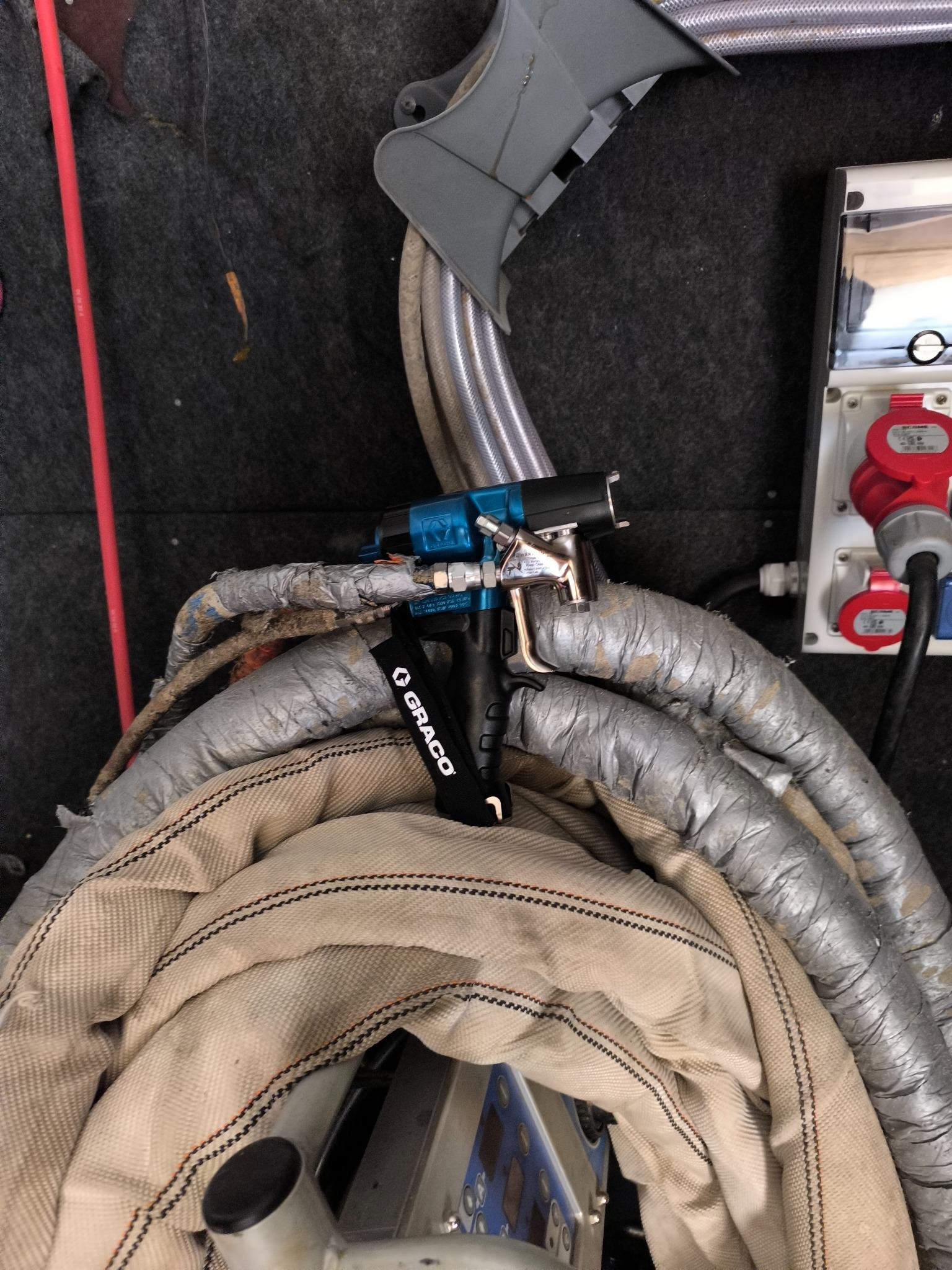 Sprzęt do natrysku pianki: pistolet natryskowy Graco na zwiniętych wężach, widoczne złącza elektryczne. Przygotowanie do aplikacji izolacji.