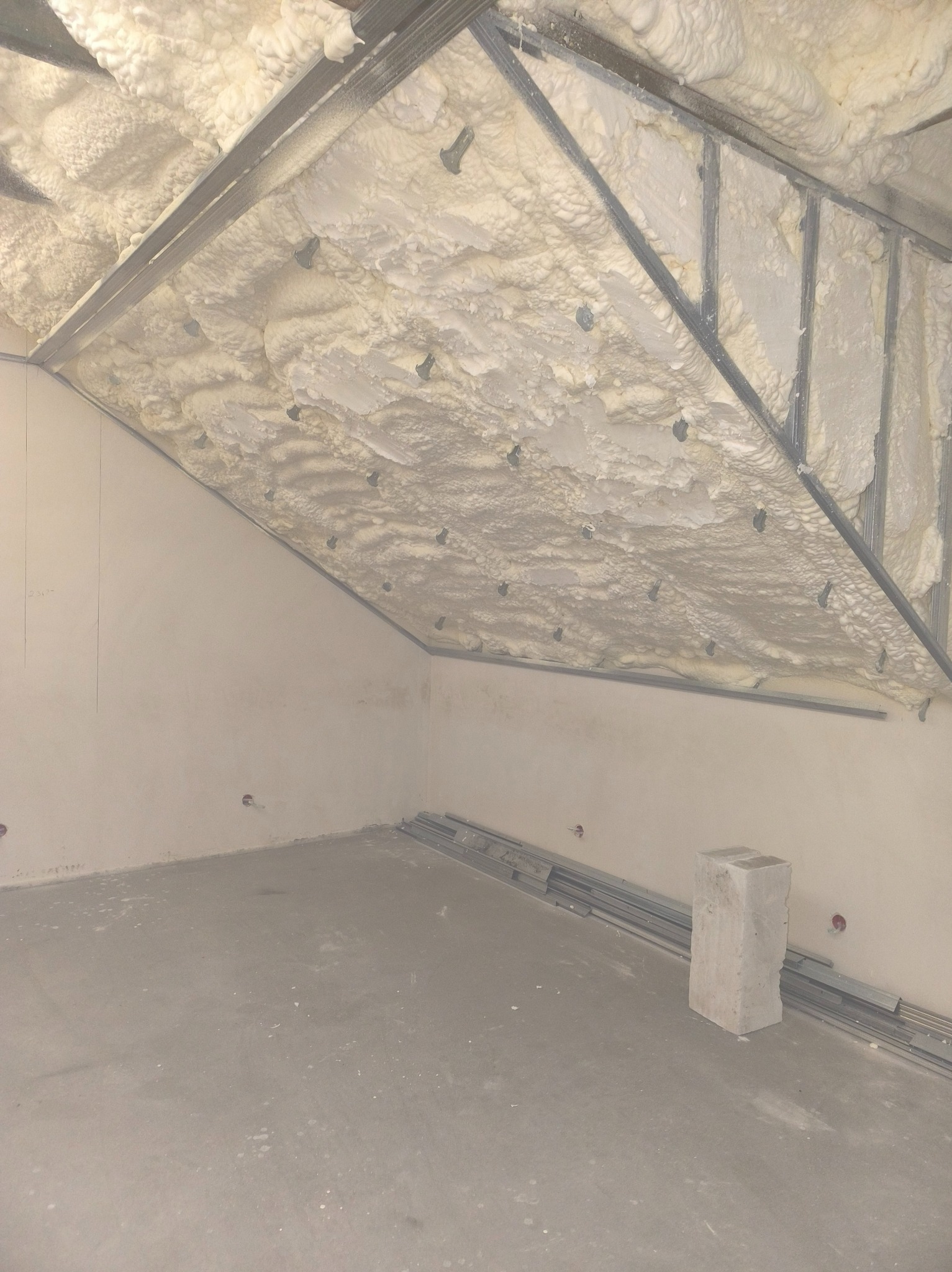 Poddasze po natrysku izolacji piankowej, widoczne metalowe profile konstrukcyjne. Biała, nierówna powierzchnia piany szczelnie wypełnia przestrzeń.
