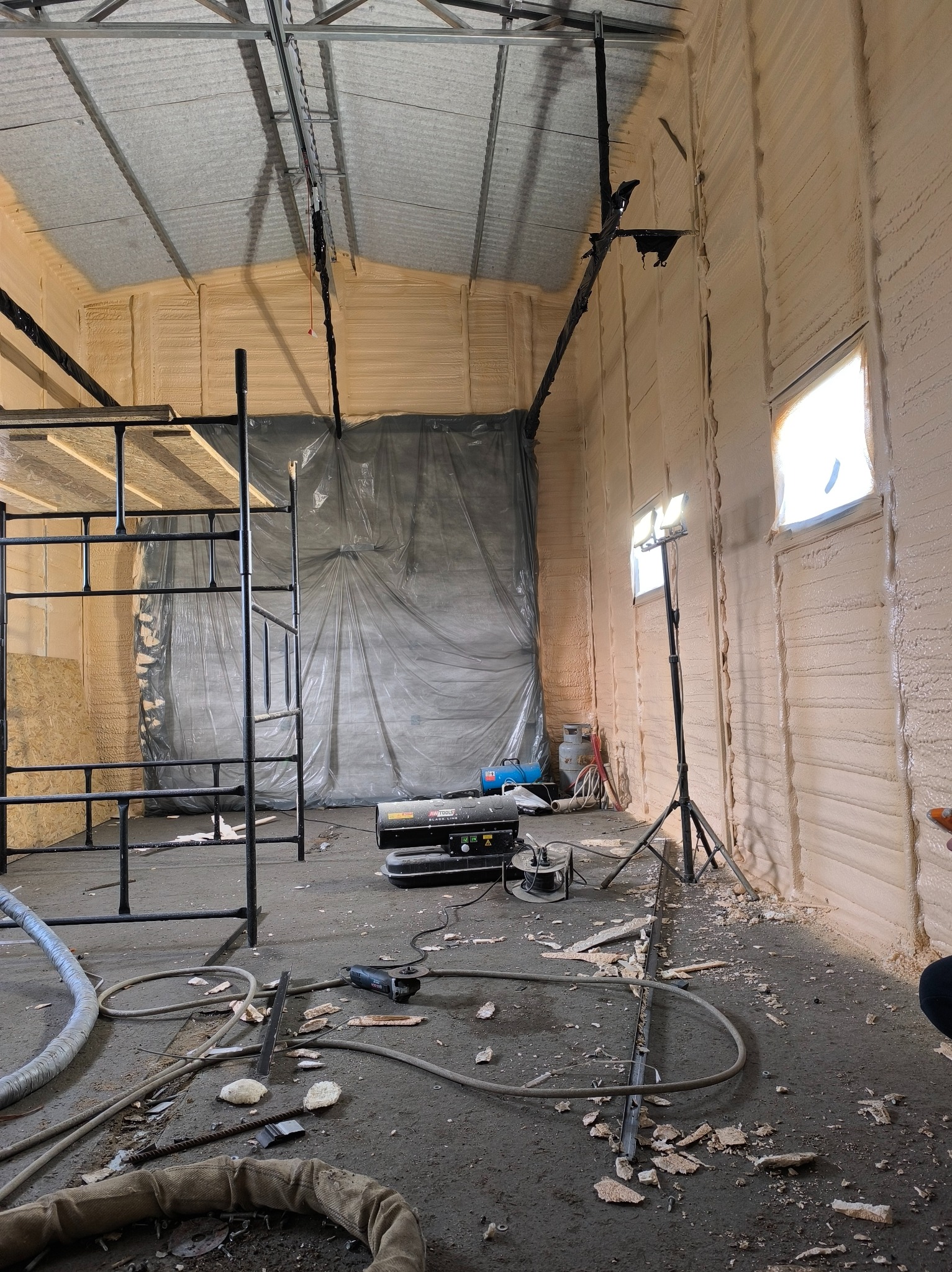 Wnętrze hali po aplikacji izolacji. Widoczne ściany pokryte pianką, rusztowanie, sprzęt roboczy i oświetlenie. Detale wykończenia i struktura piany.