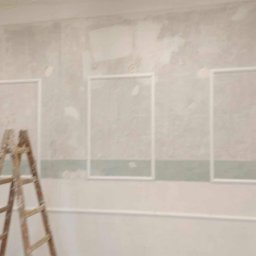 Perfect Finish - Ściana w trakcie dekorowania z zamontowanymi białymi listwami tworzącymi ramy, widoczna drewniana drabina i listwy przypodłogowe