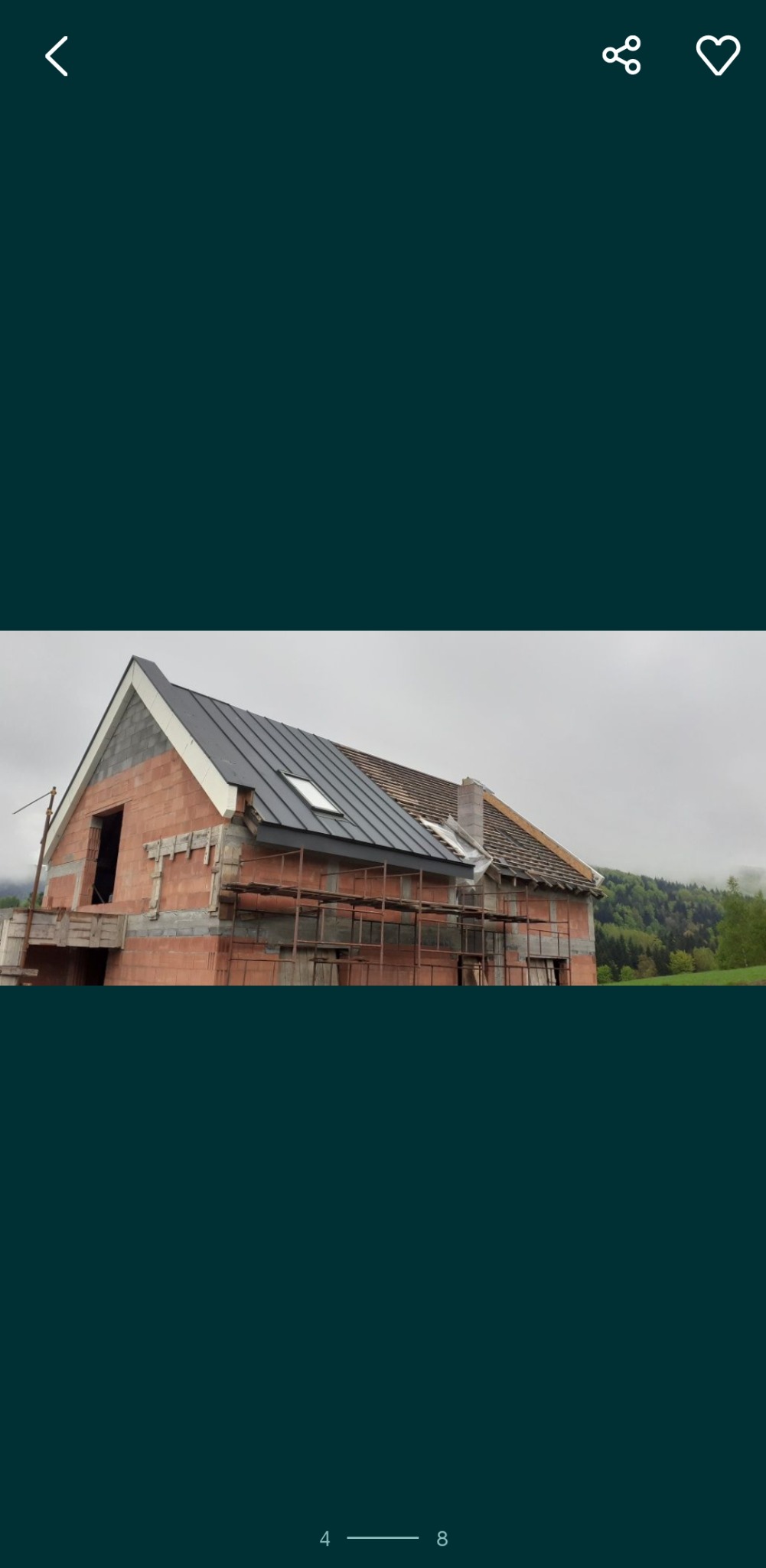 Dom w trakcie budowy z częściowo wymienionym dachem z blachy na tle zalesionego wzgórza.