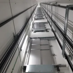 Wnętrze szybu windowego w trakcie montażu, widok z dołu, widoczne prowadnice, oświetlenie i elementy konstrukcyjne.