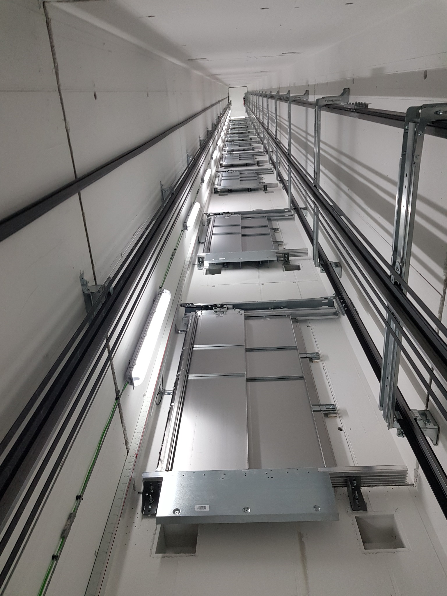 Wnętrze szybu windowego w trakcie montażu, widok z dołu, widoczne prowadnice, oświetlenie i elementy konstrukcyjne.