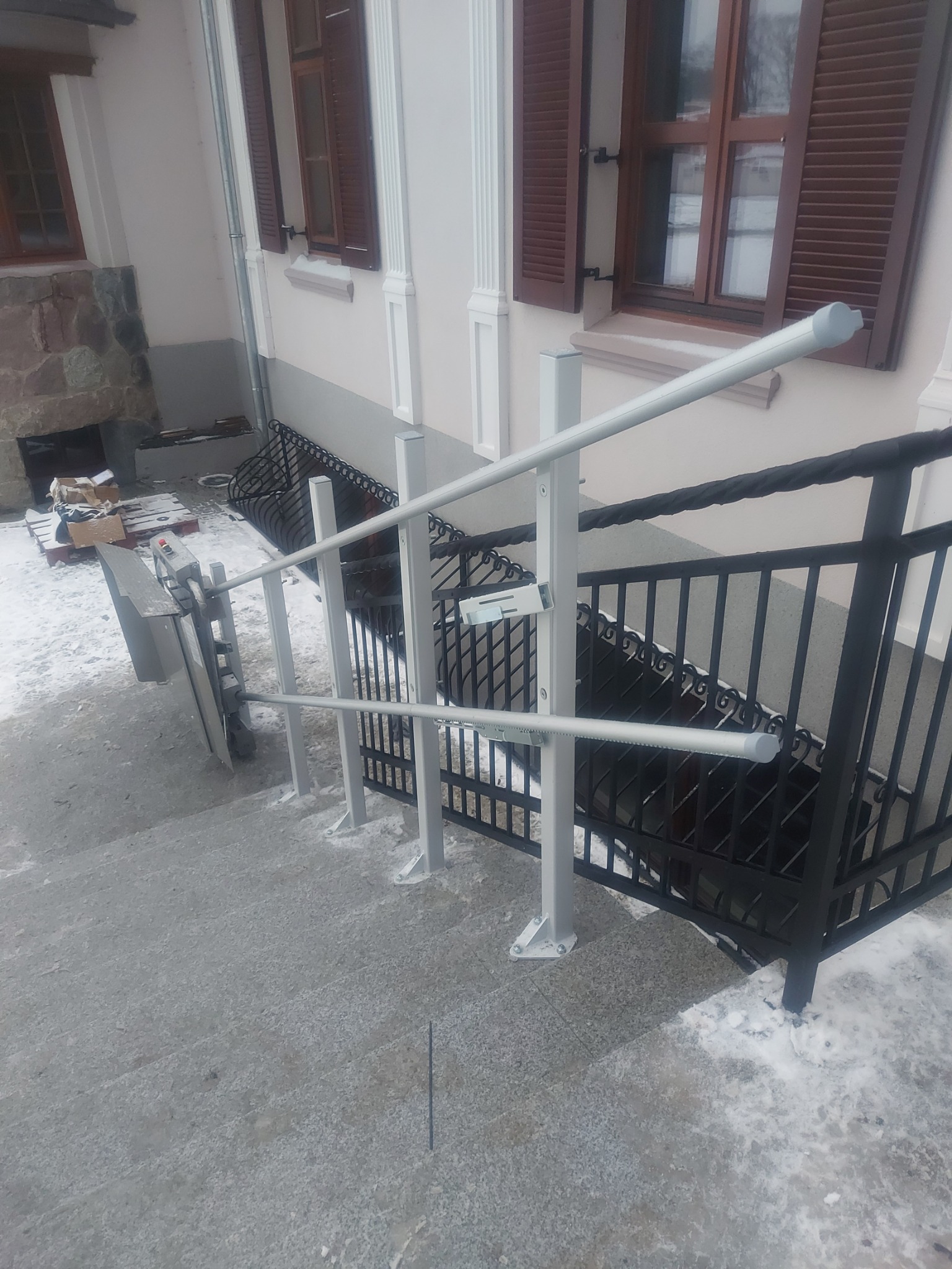 Platforma schodowa dla osób niepełnosprawnych zamontowana przy schodach zewnętrznych w Poznaniu, widoczna w zimowej scenerii.