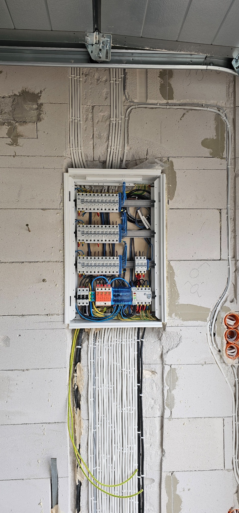 Rozdzielnia elektryczna w trakcie montażu na ścianie z betonu komórkowego, widoczne kable w listwach i peszlach oraz zabezpieczenia różnicowoprądowe i nadprądowe.