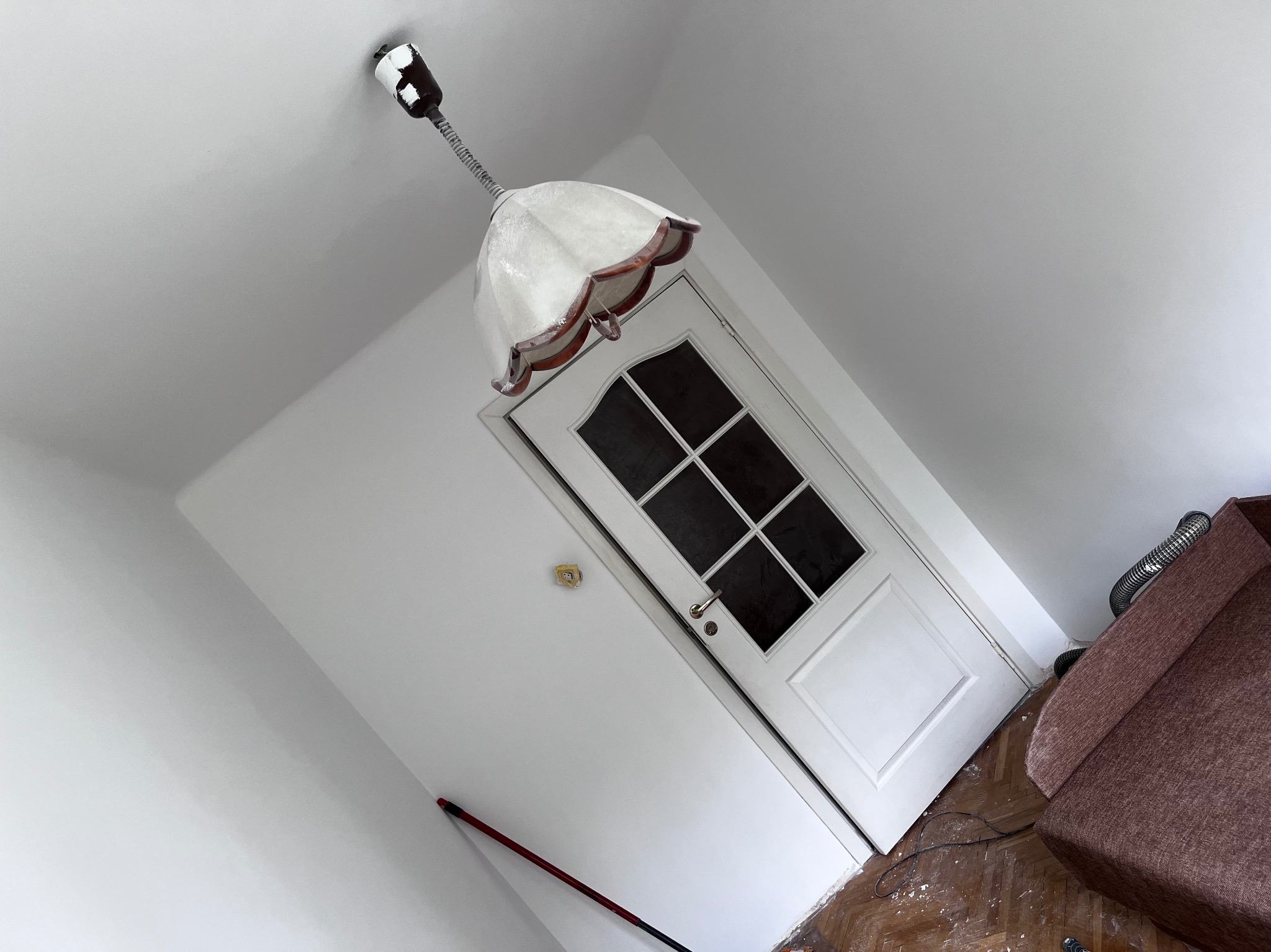 Wnętrze po świeżym pomalowaniu ścian na biało, widoczna biała stolarka drzwiowa z szybami, zabezpieczona podłoga i lampa w stylu retro.