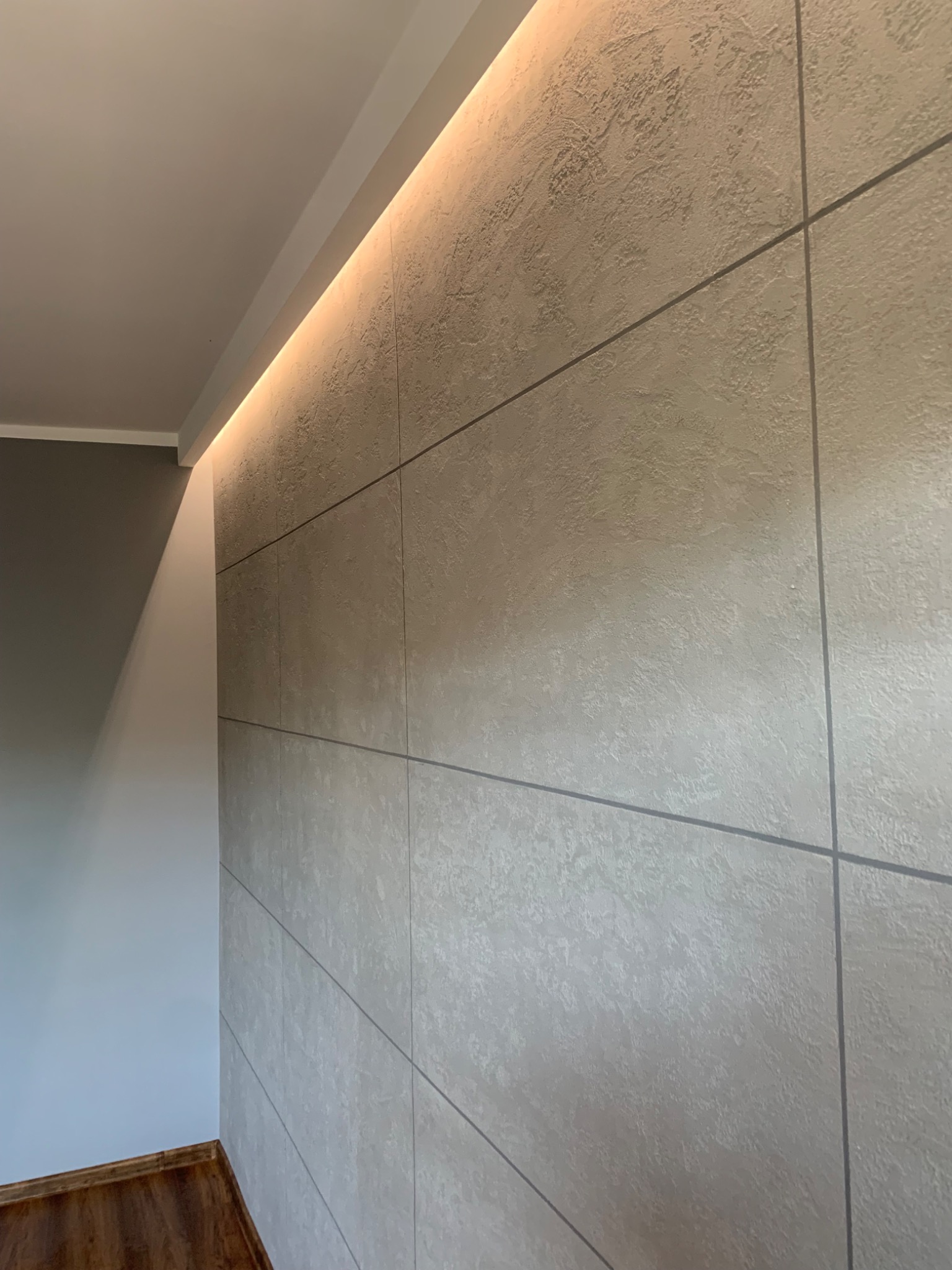 Ściana wykończona panelami z dekoracyjną fakturą, podświetlona listwą LED, widok z dołu, drewniana podłoga.