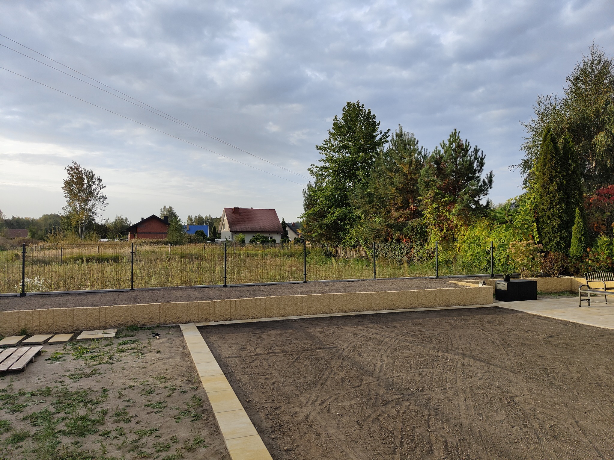 Przygotowany teren pod przyszły trawnik z obrzeżami z kostki, widoczny dom w tle za ogrodzeniem.
