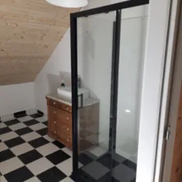 Nowoczesna łazienka na poddaszu z kabiną prysznicową z czarną ramą, umywalką na drewnianej komodzie i białą lampą wiszącą, wykończona w czarno-białą szachownicę.