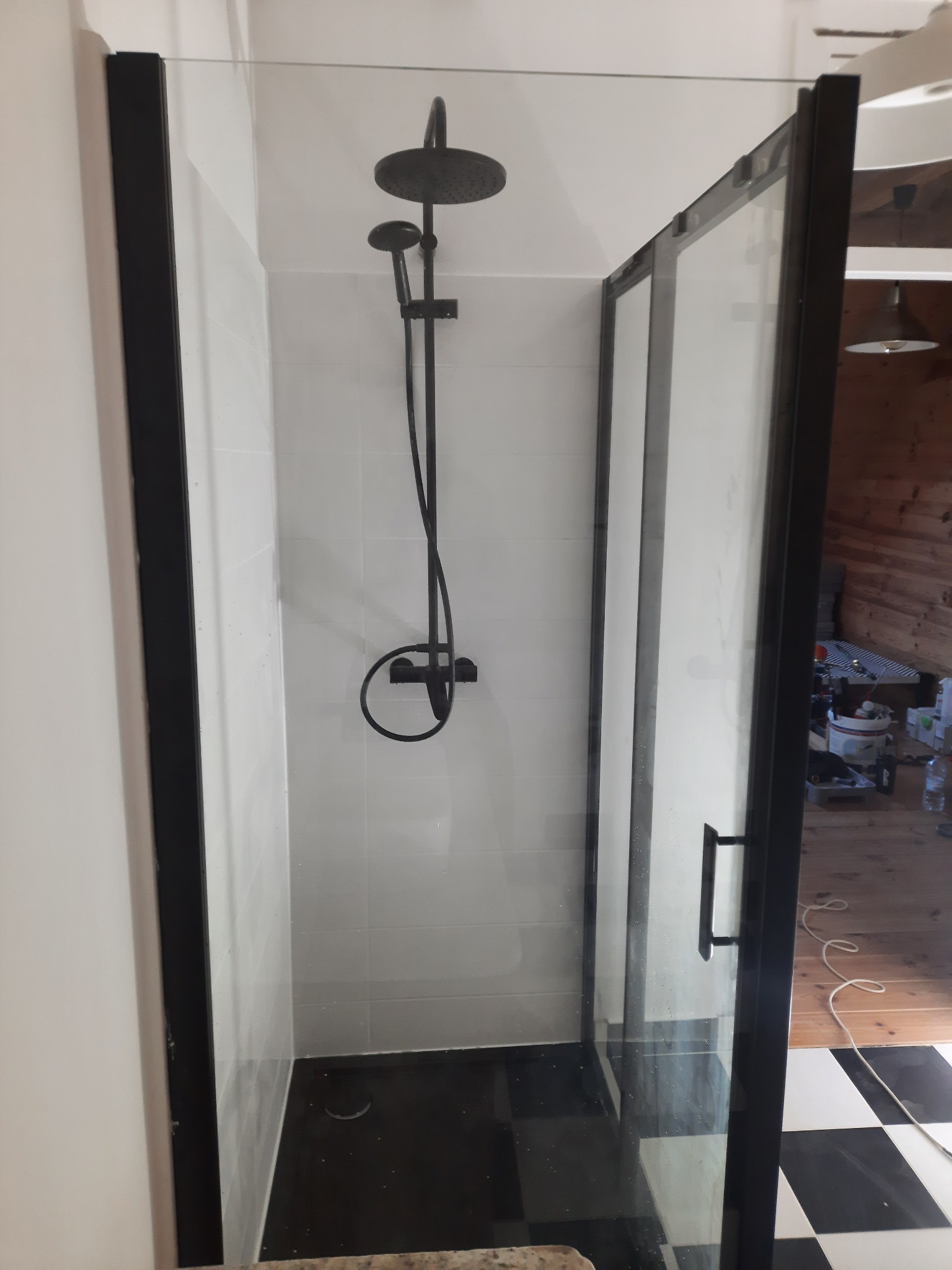 Nowoczesna kabina prysznicowa z czarną armaturą i czarnymi profilami, widok na wnętrze kabiny z czarno-białą szachownicą na podłodze i białe płytki na ścianach.