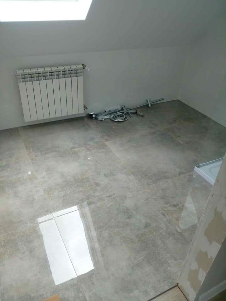 Płytki podłogowe w łazience na poddaszu, widoczny grzejnik i instalacja hydrauliczna przed montażem armatury.