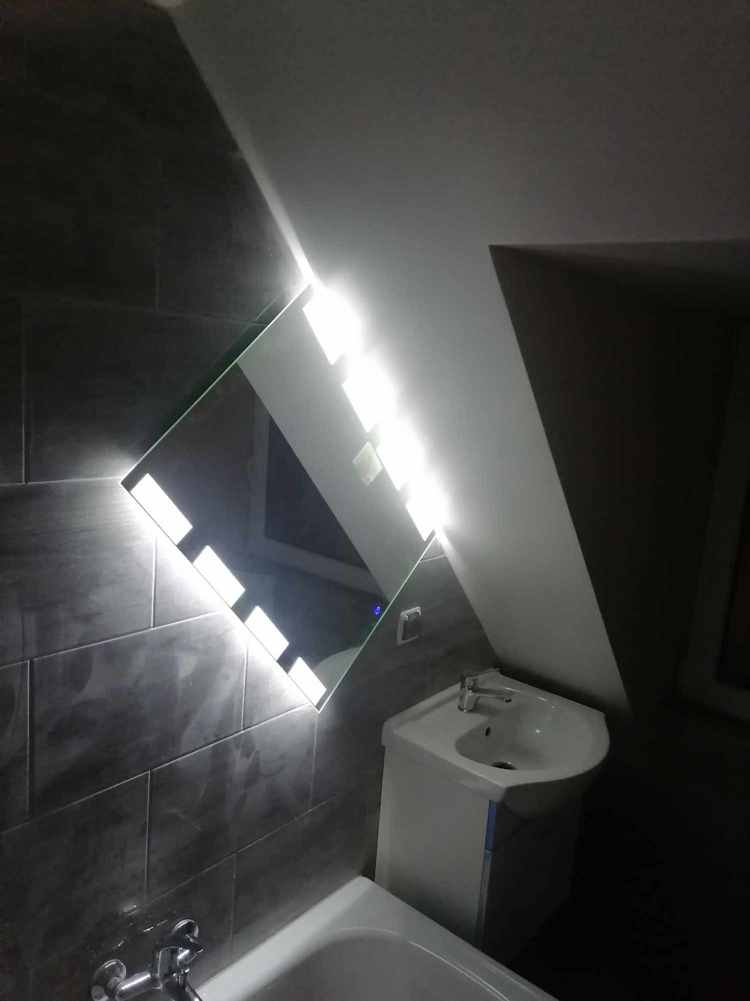 Nowoczesna łazienka z umywalką na szafce i podświetlanym lustrem LED, szare płytki na ścianie, widok z dołu.