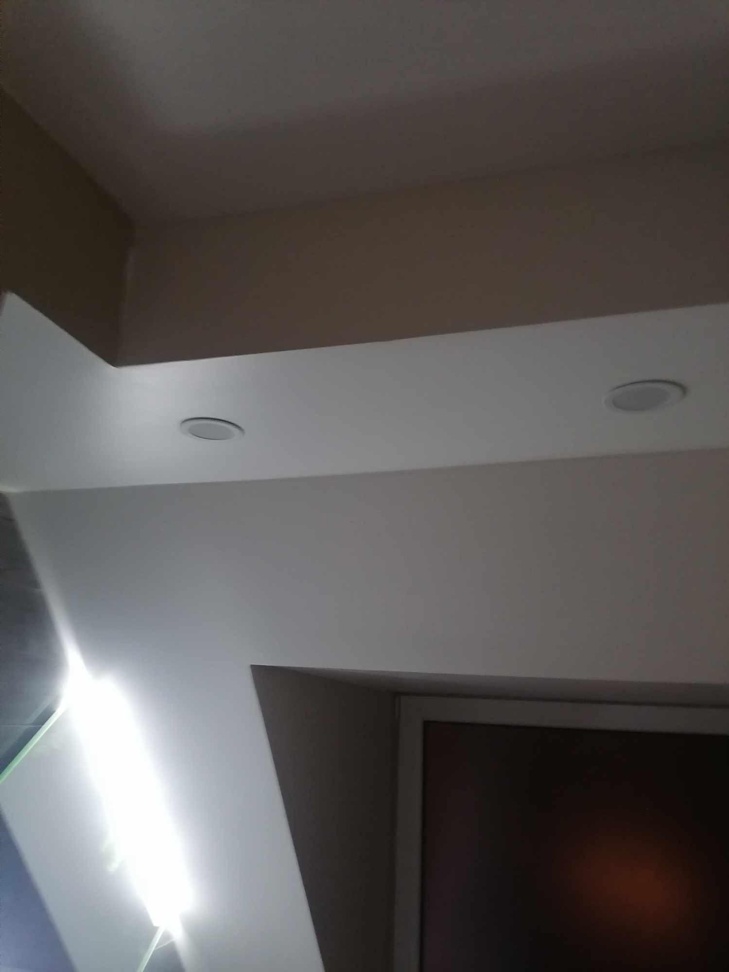 Biały sufit podwieszany z wbudowanymi okrągłymi lampami LED, widoczny fragment ściany w kolorze beżowym i fragment okna.