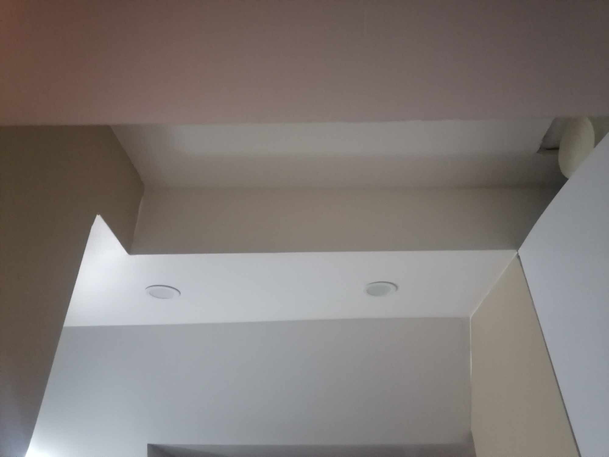 Widok fragmentu sufitu i ścian po malowaniu na biało i beżowo, z zamontowanymi dwoma okrągłymi lampami sufitowymi.