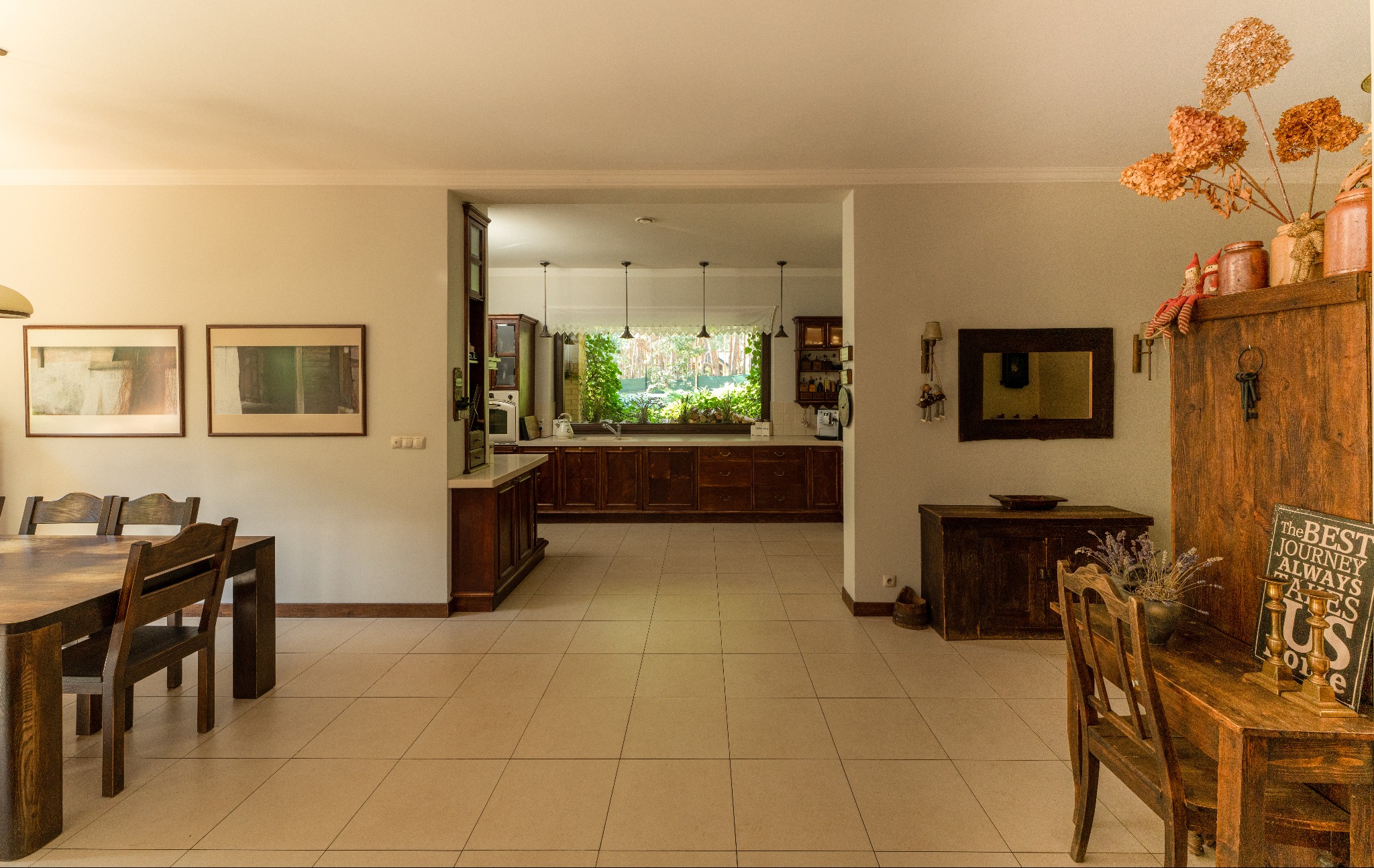 Przestronne wnętrze domu z otwartą kuchnią, drewnianymi meblami i dekoracjami w stylu rustykalnym, widok na zielony ogród przez okno.