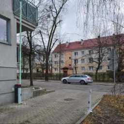 Szlaban automatyczny z podświetleniem LED przy wjeździe na osiedle, szary budynek w tle, przejeżdżający samochód.