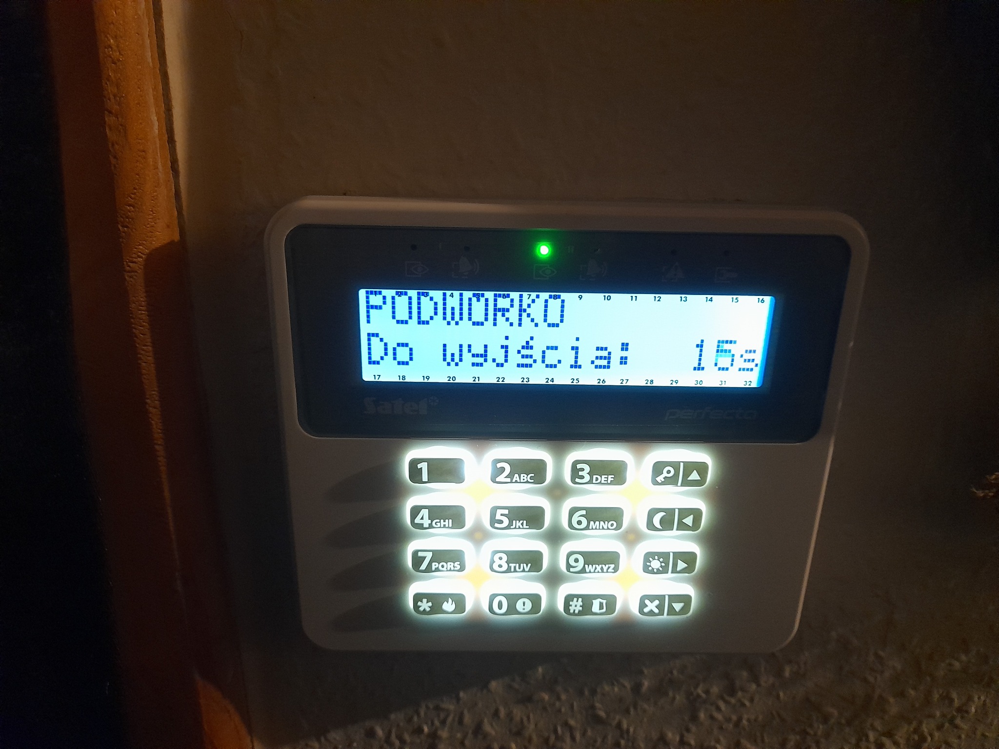 Panel sterowania alarmem Satel Perfecta z podświetlanymi przyciskami, wyświetlający komunikat 'PODWORKO Do wyjścia: 15s' i świecącą się zieloną diodą.