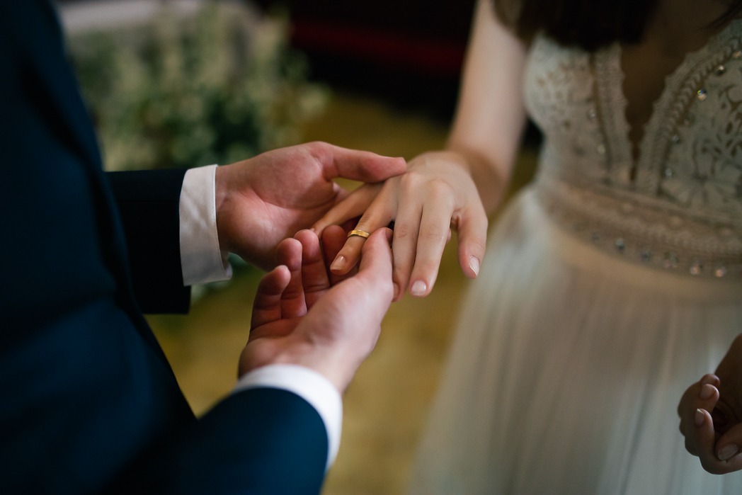 Moment zakładania złotej obrączki na palec panny młodej w sukni ślubnej, uchwycony przez fotografa ślubnego z Redzikowa.