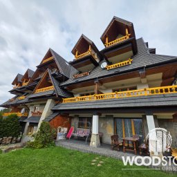 Paweł Śliwiński - Rozległy dom w stylu góralskim z drewnianymi balkonami i balustradami w kolorze żółtym, widok z poziomu trawnika, pochmurne niebo w tle. Charakterystyczna architektura.