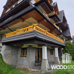 Paweł Śliwiński - Wielopoziomowy budynek z balkonami o żółtych balustradach, wykończony kamieniem i drewnem, otoczony zielenią. Widoczne detale architektoniczne i naturalne materiały.