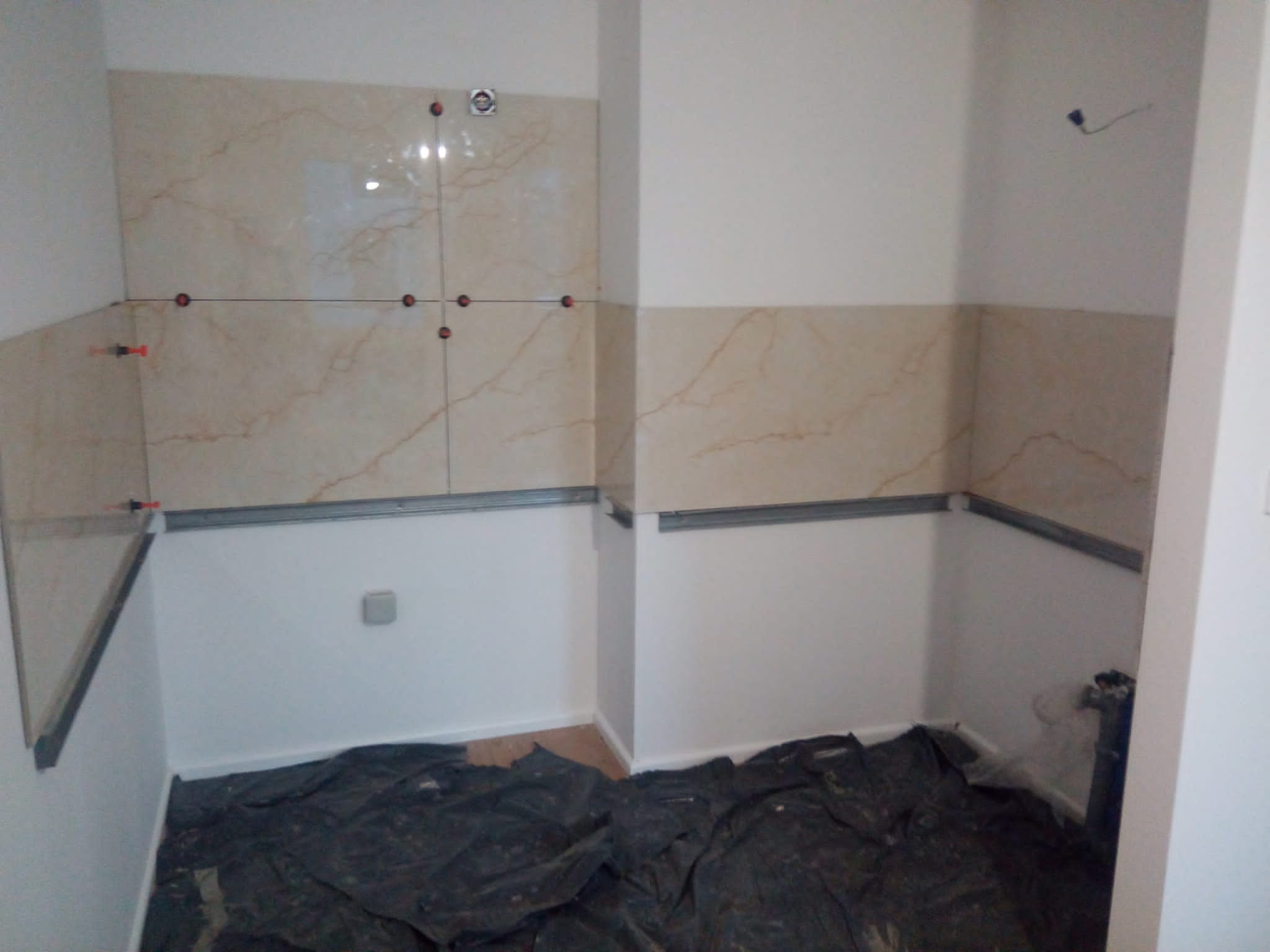 Wnętrze łazienki w trakcie układania płytek ściennych z marmurkowym wzorem, widoczne listwy montażowe i krzyżyki dystansowe, podłoga zabezpieczona folią.